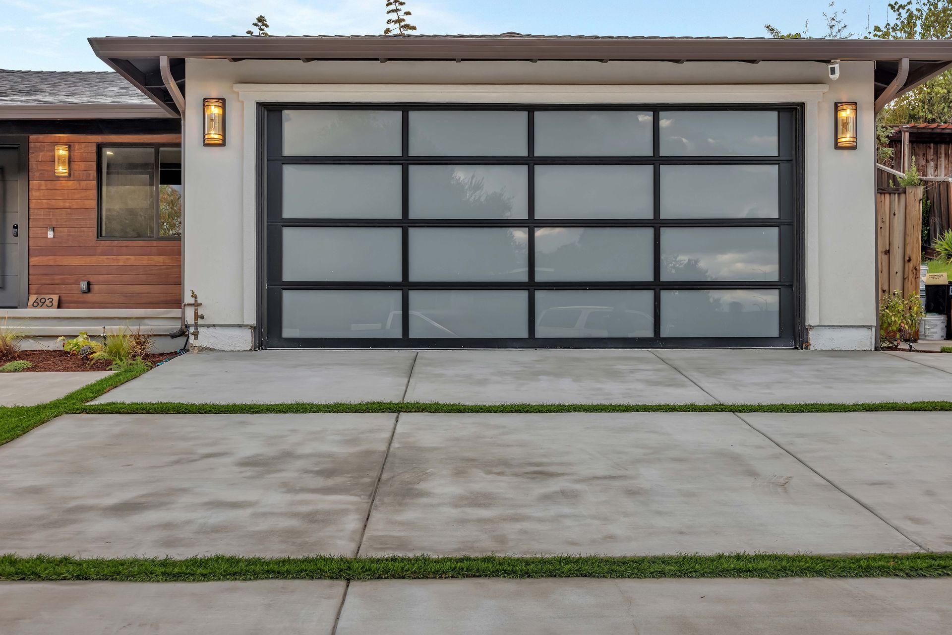 Modern garage with frosted glass door, concrete driveway, and landscaped accents.