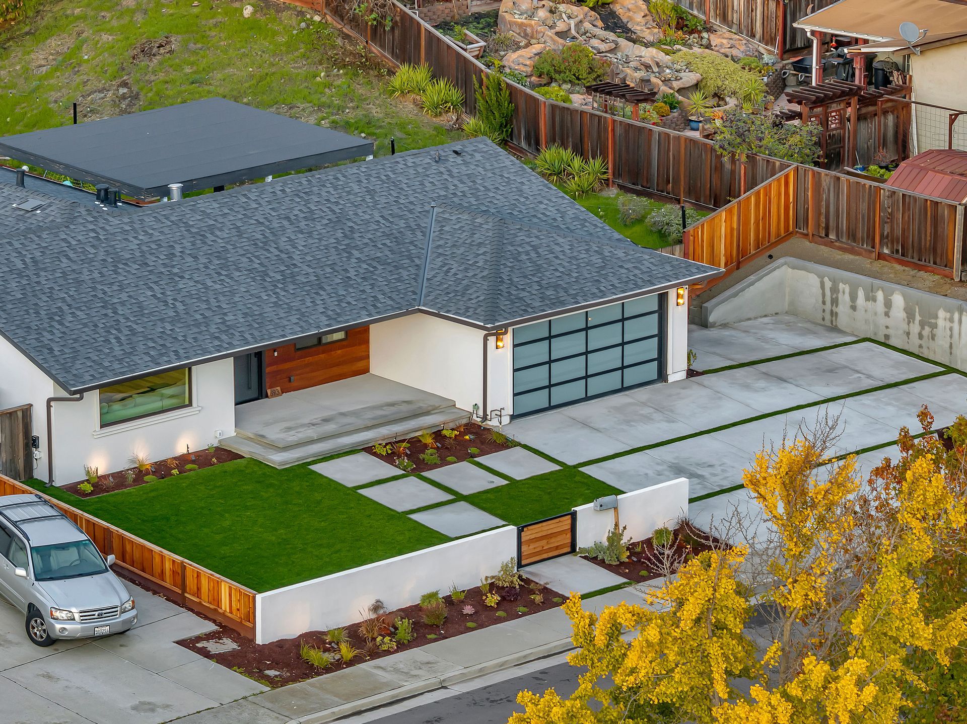 Modern white house with gray roof, glass garage door, and manicured landscaping.