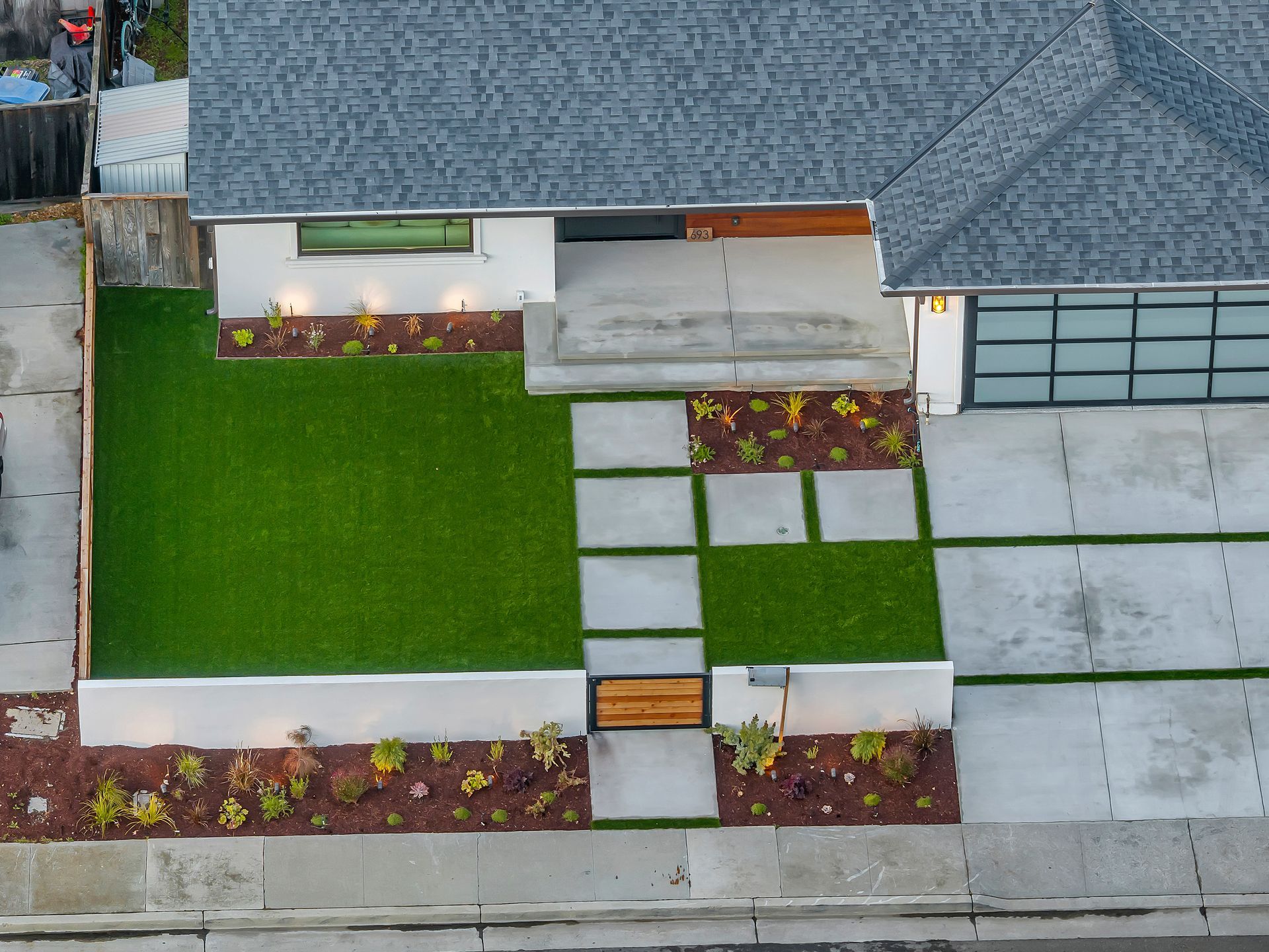 Overhead view of a modern house with a green lawn, concrete path, and glass garage door.