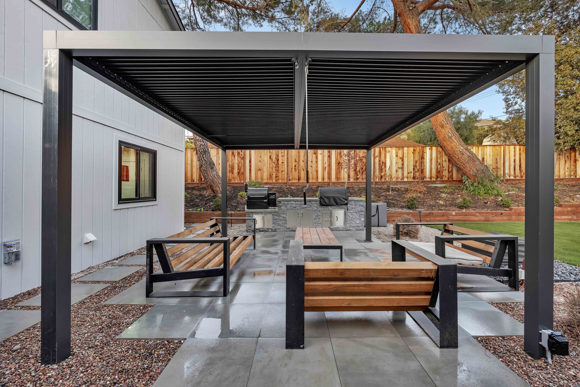 White building with a wooden door and black-framed glass doors, surrounded by a concrete patio and a wooden fence.