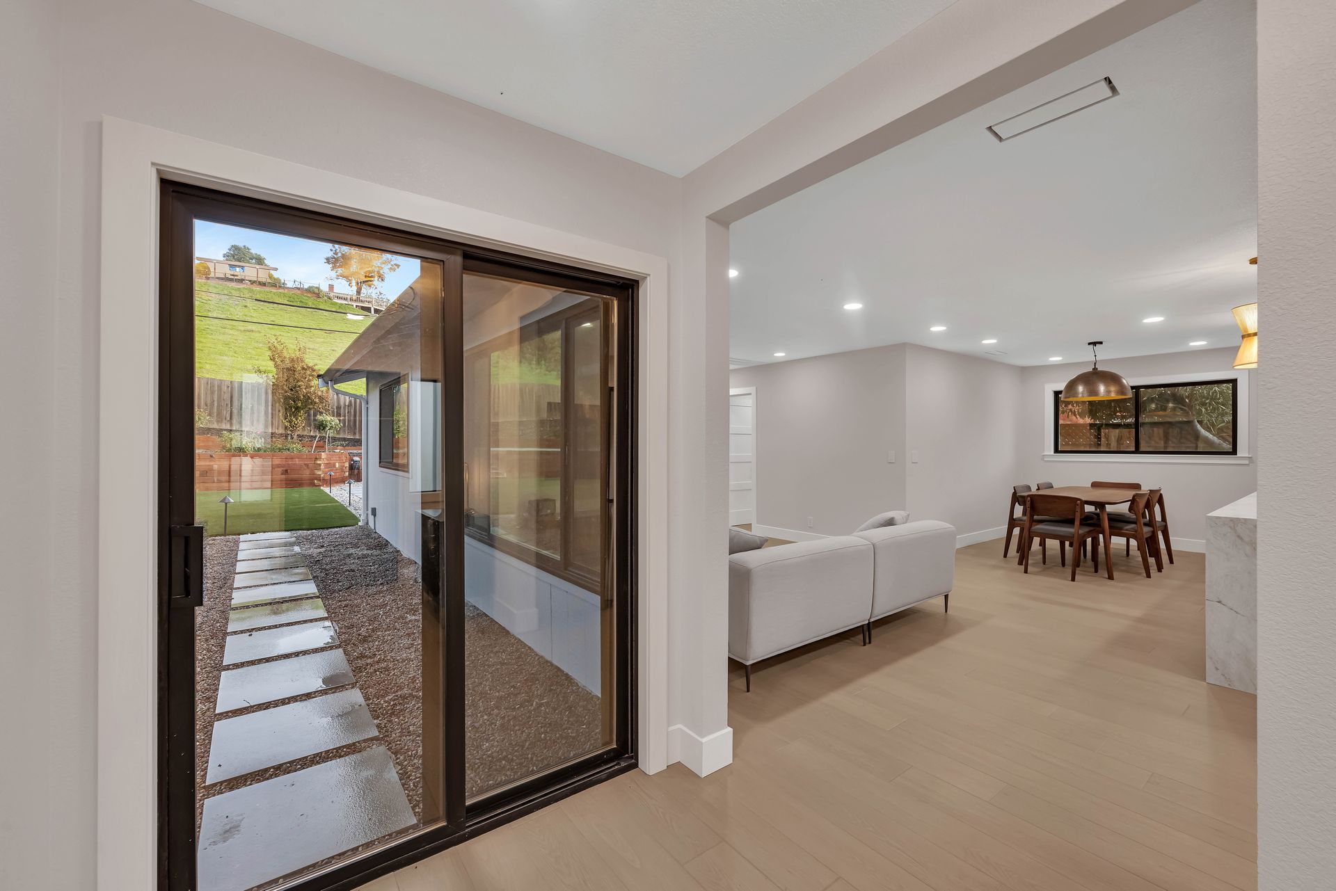Interior view: sliding glass doors open to a backyard. Inside, a living room with a couch and dining area.