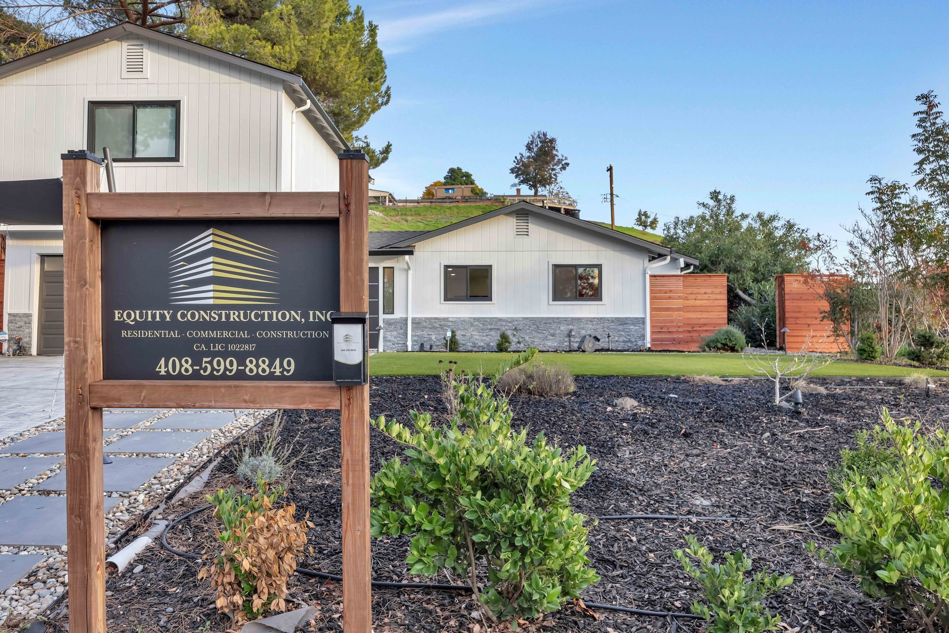 Sign for Myron Construction Company in front of a white house with a green roof, black mulch, and a driveway.