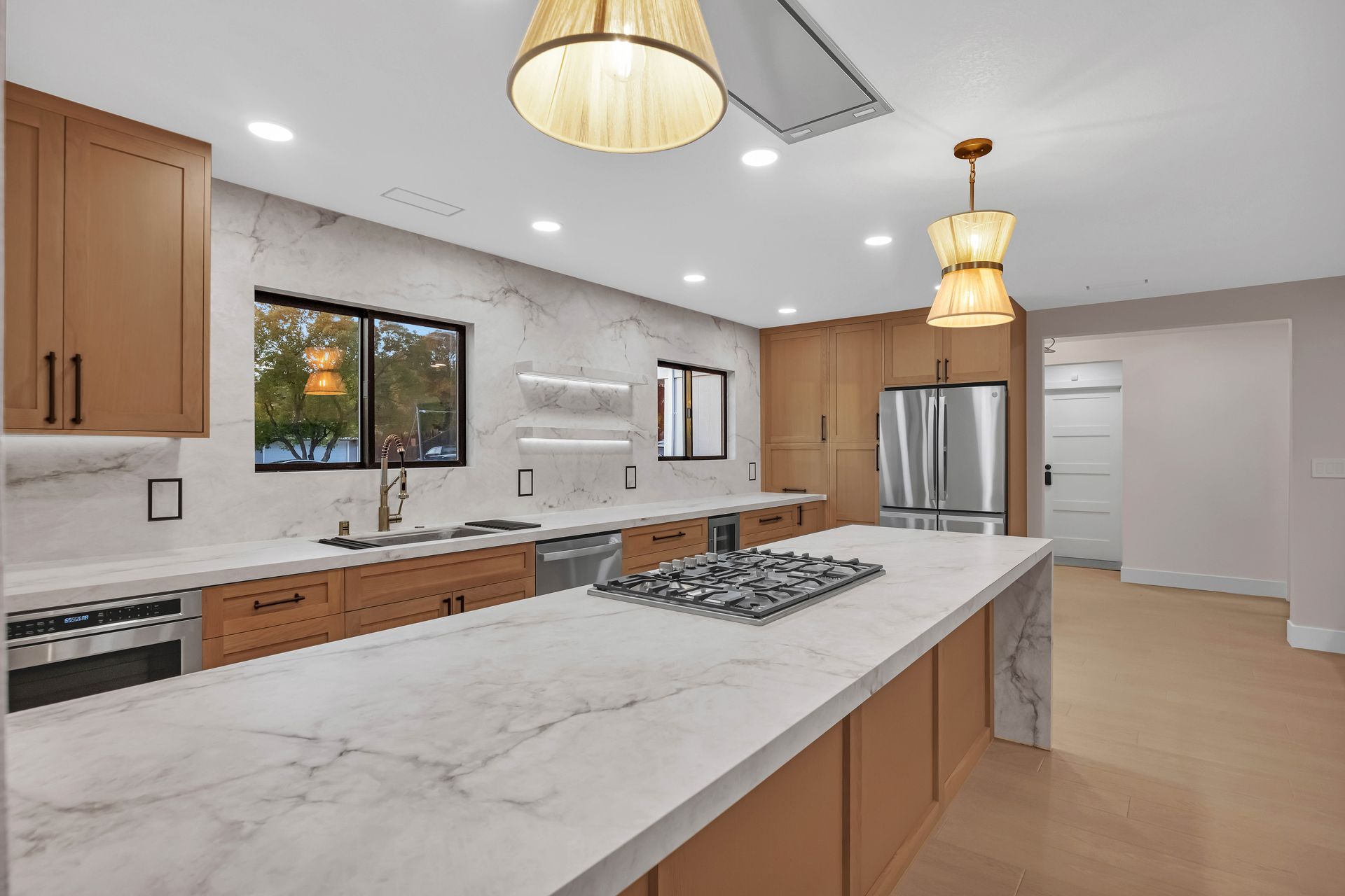 Modern kitchen with marble countertops, wood cabinets, and pendant lights.