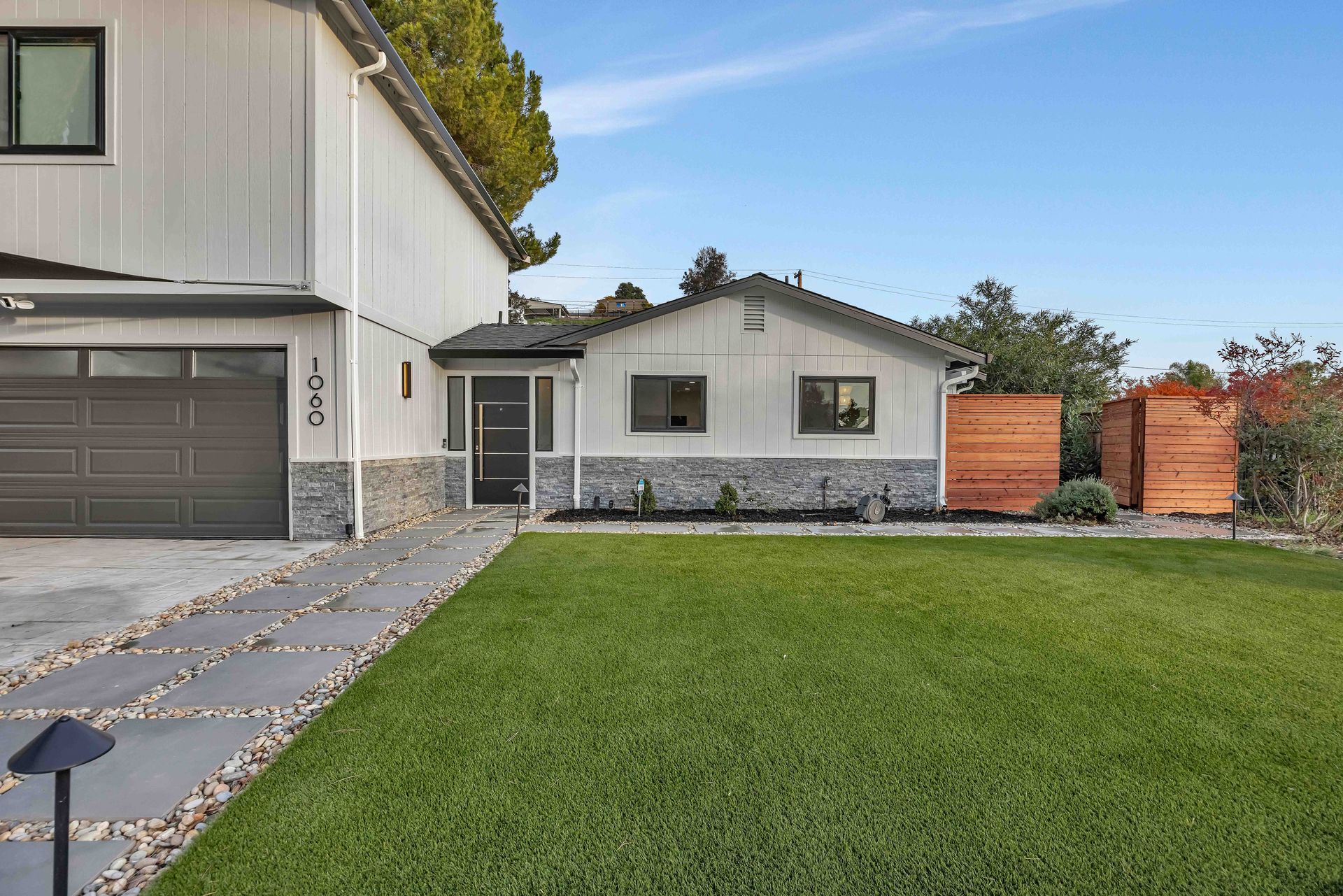 Modern gray-tiled shower with glass door, black fixtures, built-in bench, and small window.