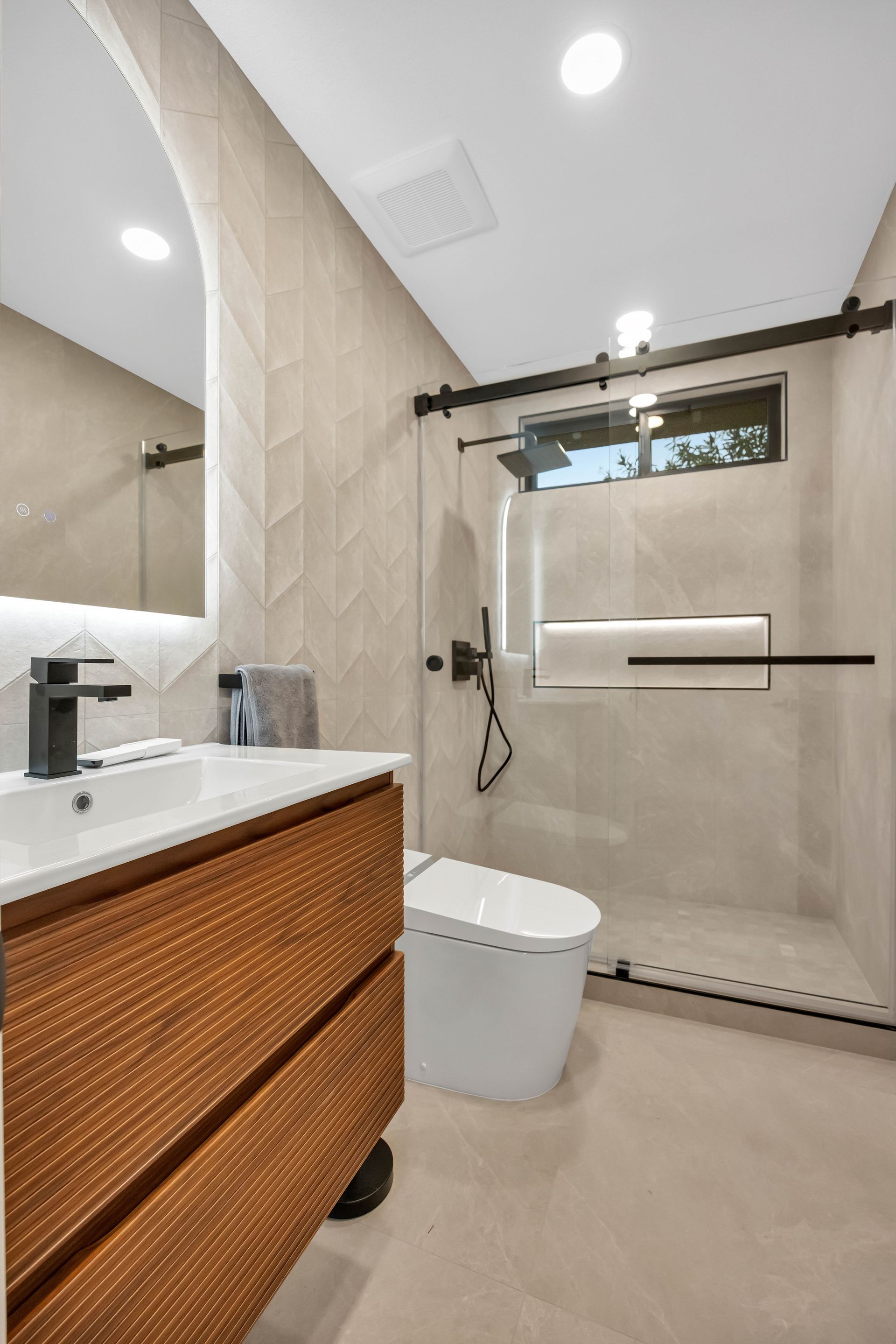 Modern shower with glass door, black fixtures, and built-in shelf. Beige tile walls.