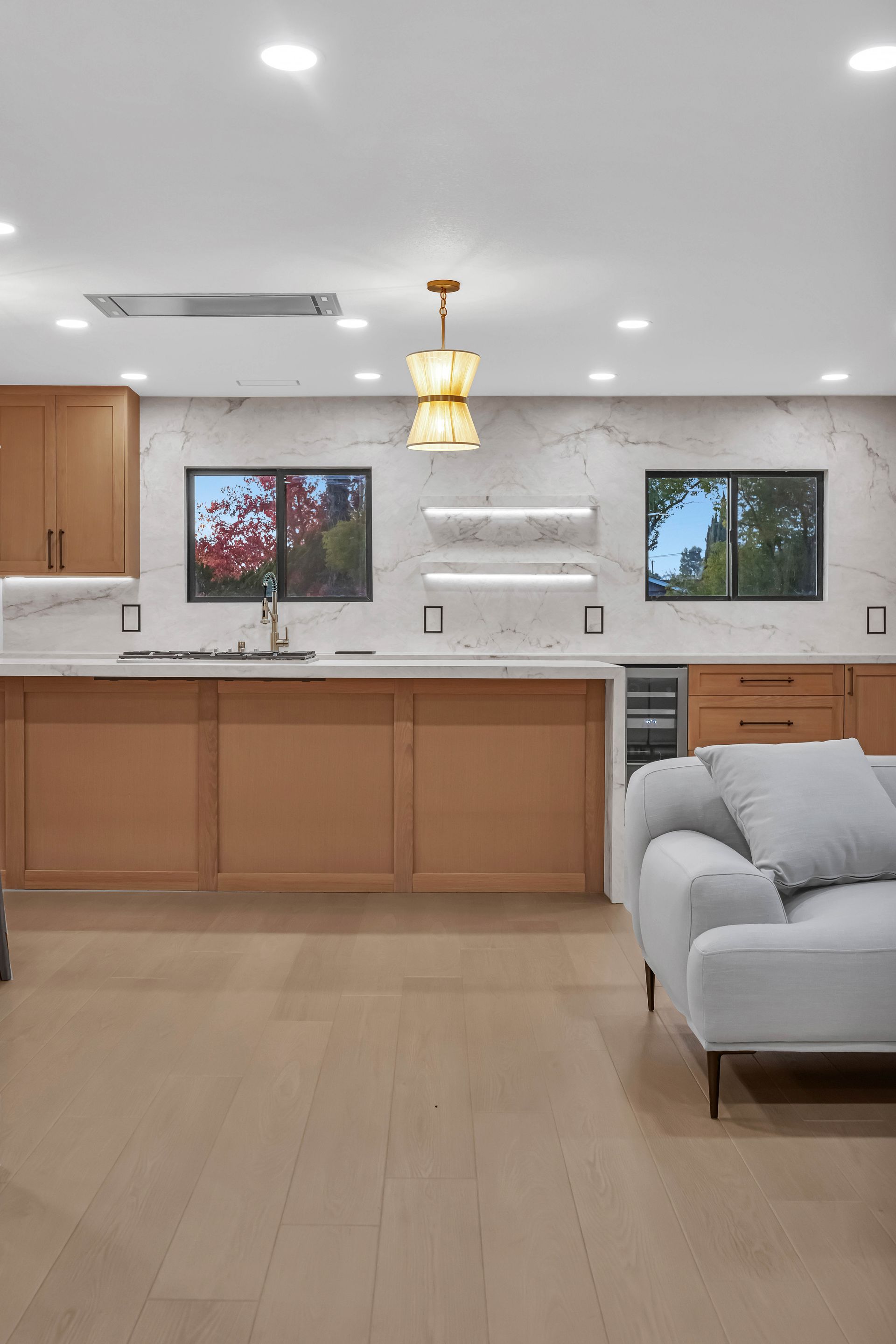 Modern kitchen with light wood cabinets, marble backsplash, and a light gray sofa.