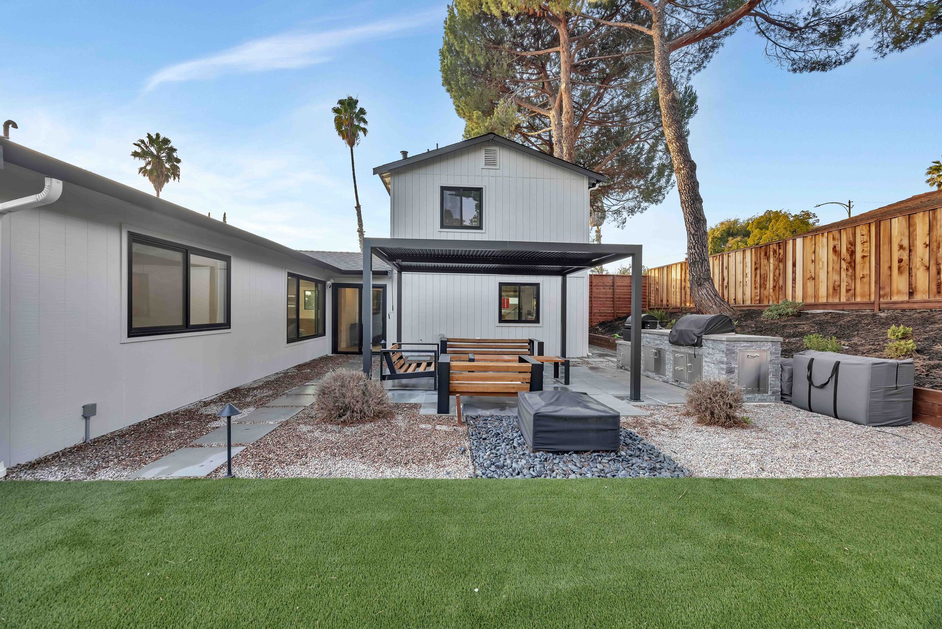 Backyard with seating area, fire pit, and a two-story building in the background. Artificial turf lawn.