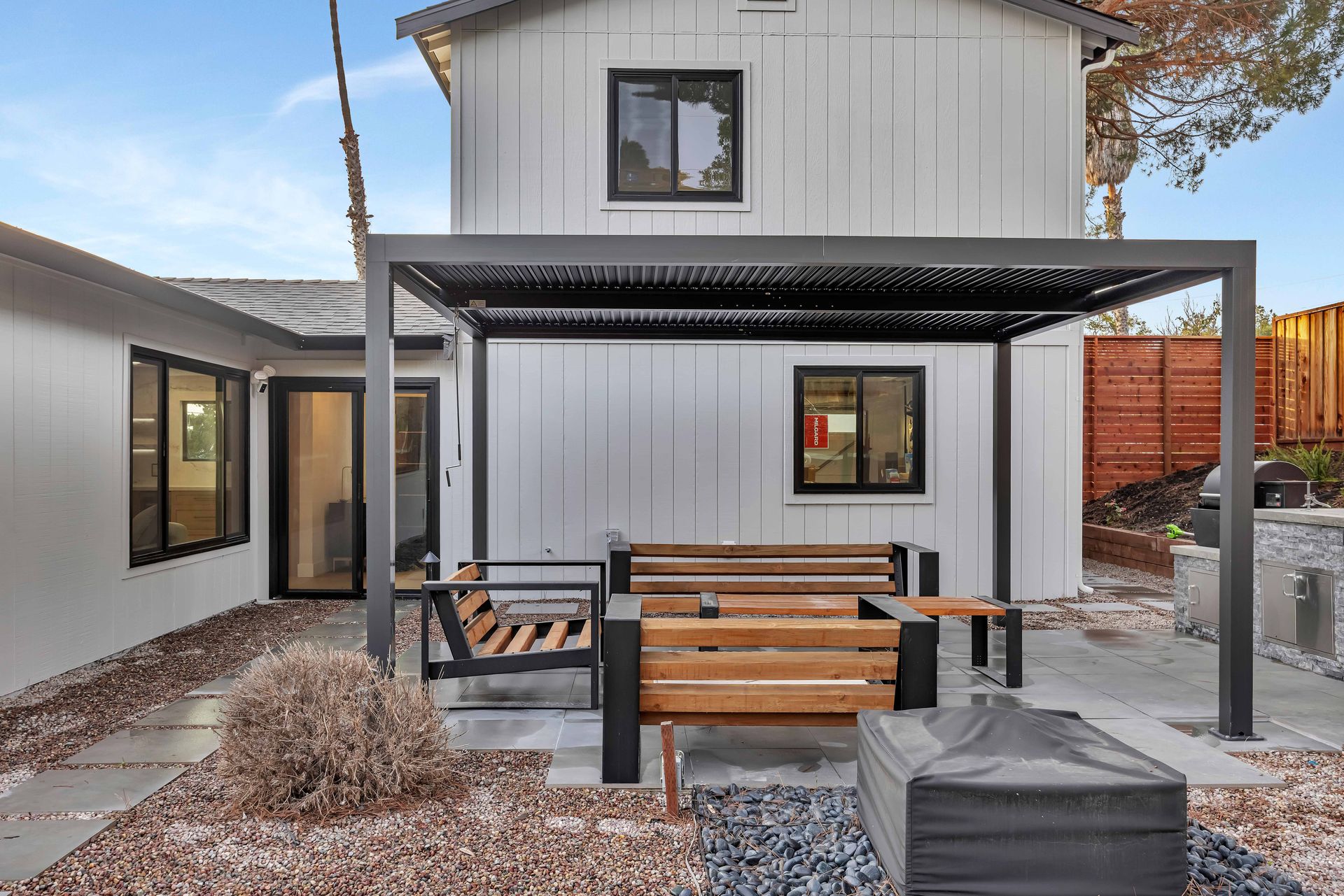 White house exterior with patio, pergola, and wooden seating.