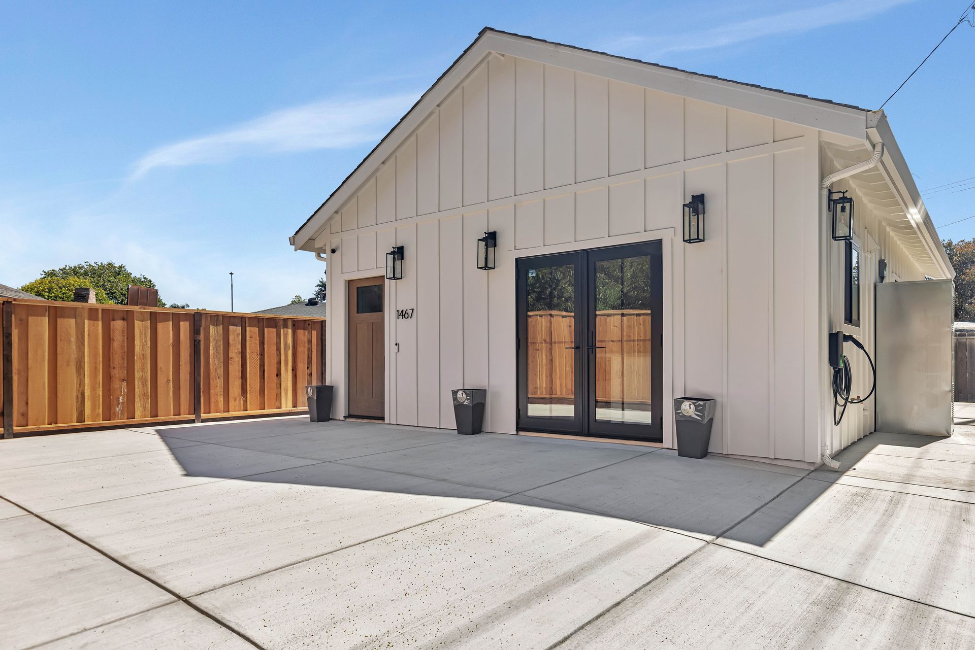 White building with dark-framed double doors, matching side door, and wooden fence, set against a blue sky.