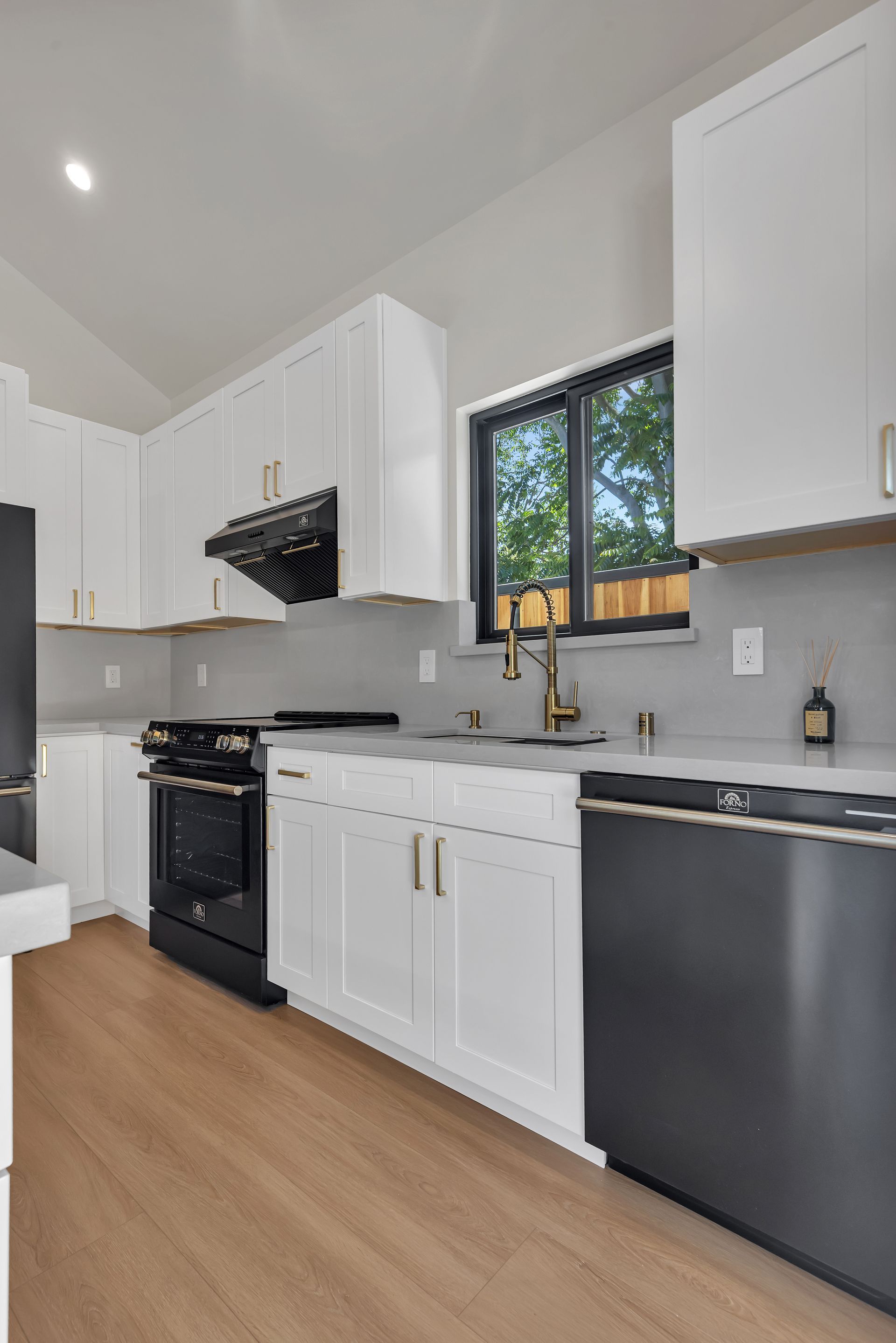 Modern kitchen with white cabinets, black appliances, light wood floors, and a window.