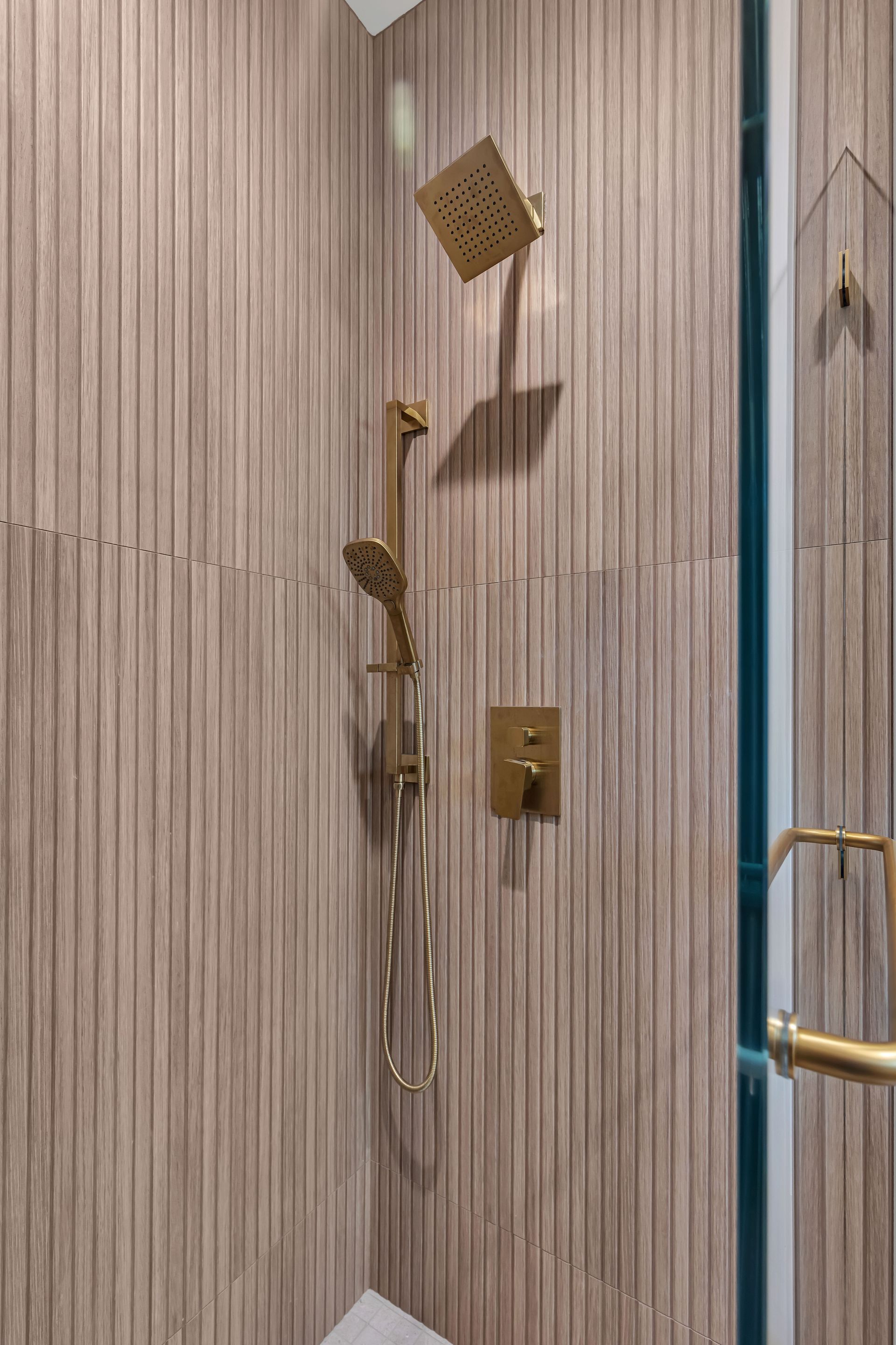 Gold shower fixtures on textured beige wall in bathroom. Glass door frame on right.