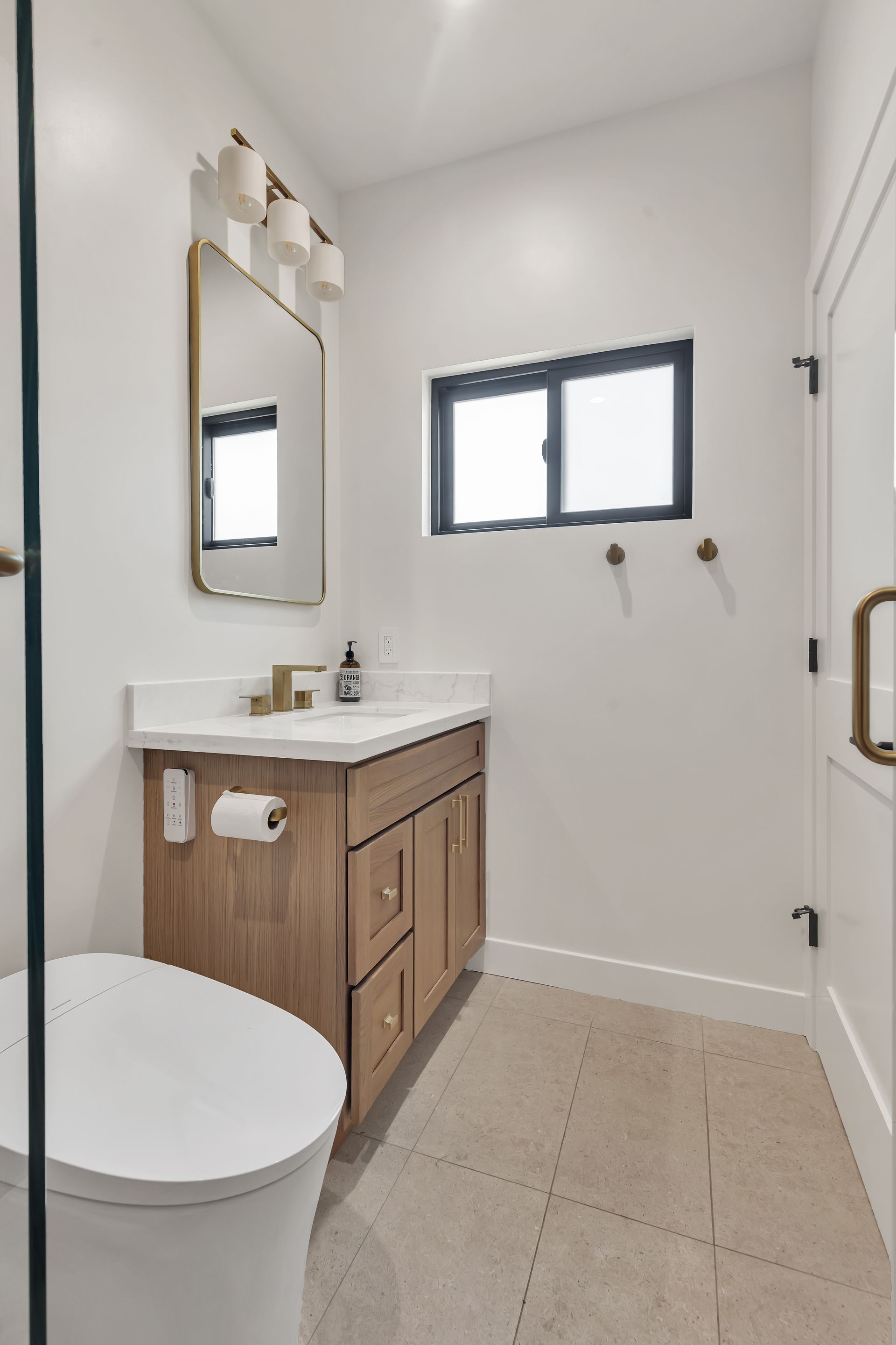 Small bathroom with a light wood vanity, white toilet, and gold accents.