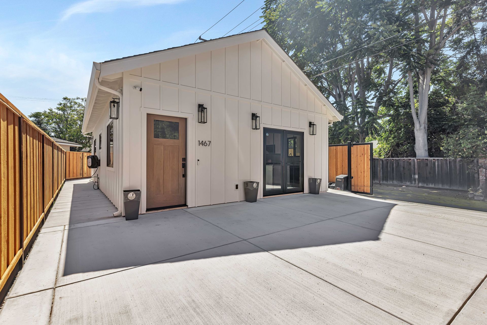 Outdoor patio with white building, gray sofa, chairs, and coffee table on concrete. Wooden fence surrounds.