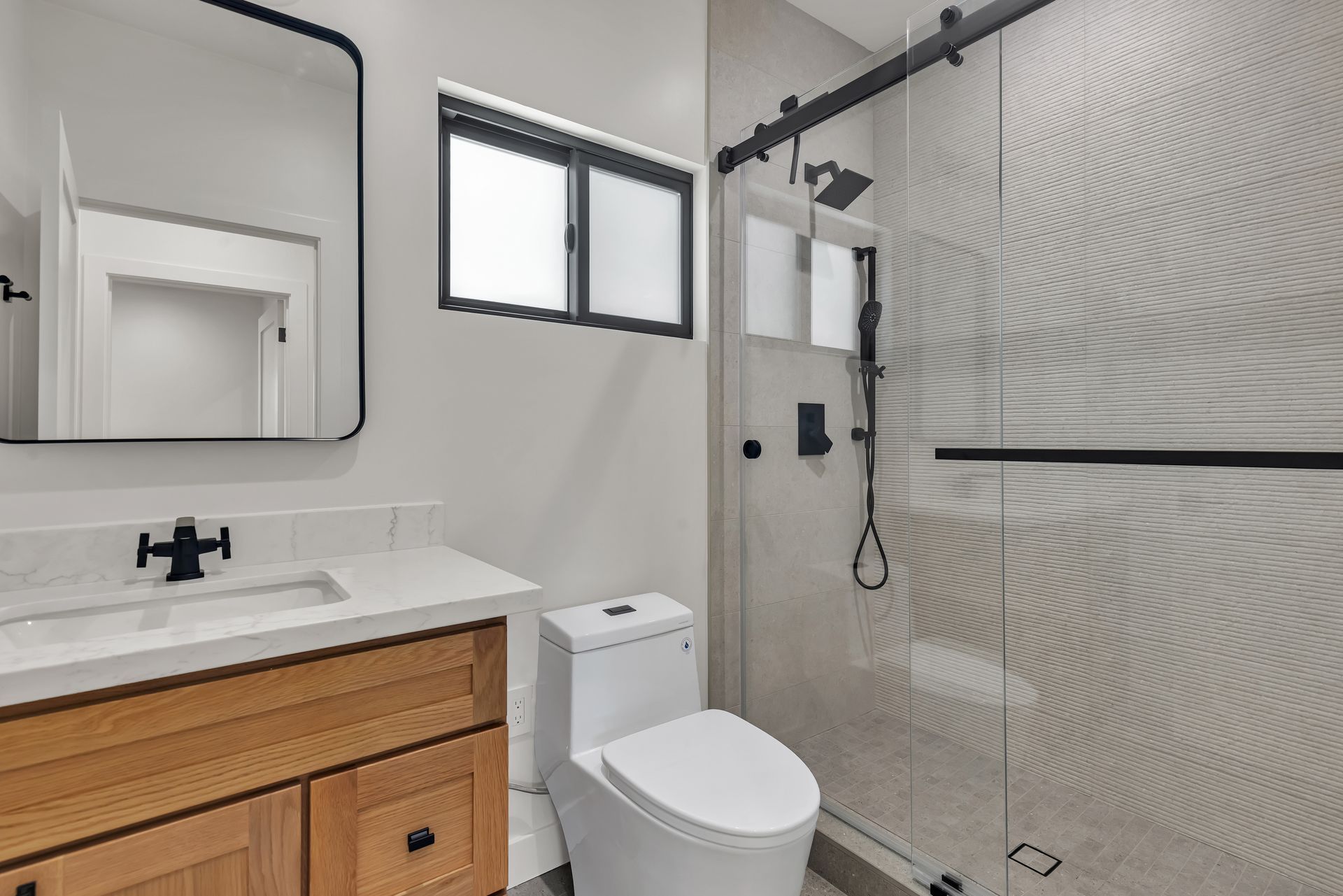 Modern bathroom with wood vanity, white toilet, and glass shower.