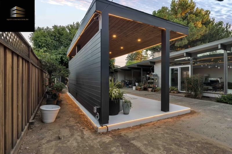 Modern outdoor patio with black siding, wood-toned ceiling, and recessed lighting.