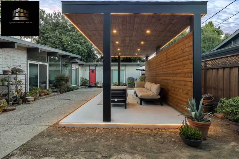 Backyard patio with wooden ceiling, black supports, seating, and ambient lighting.
