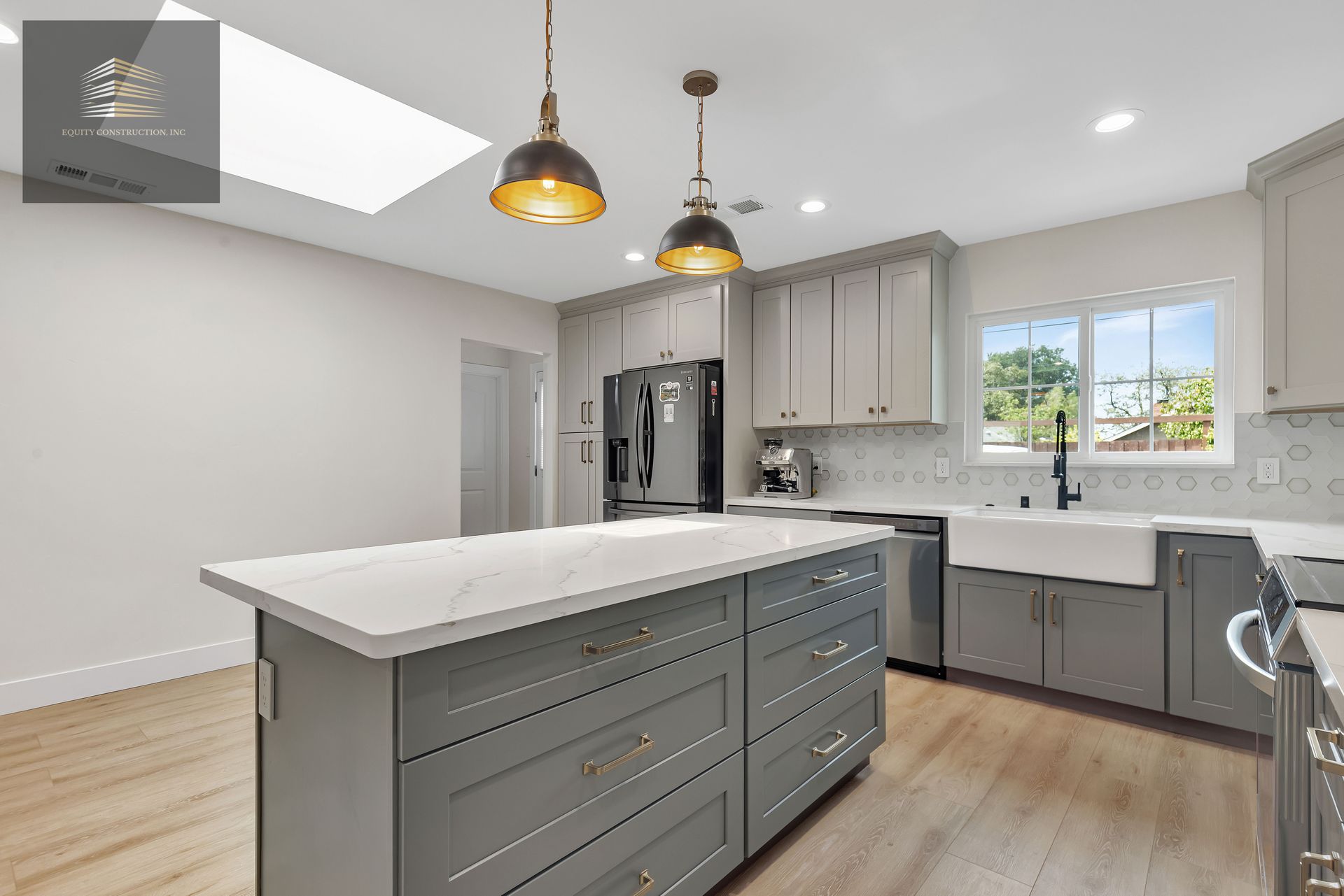 Gray and white kitchen with island, pendant lights, and stainless steel appliances.