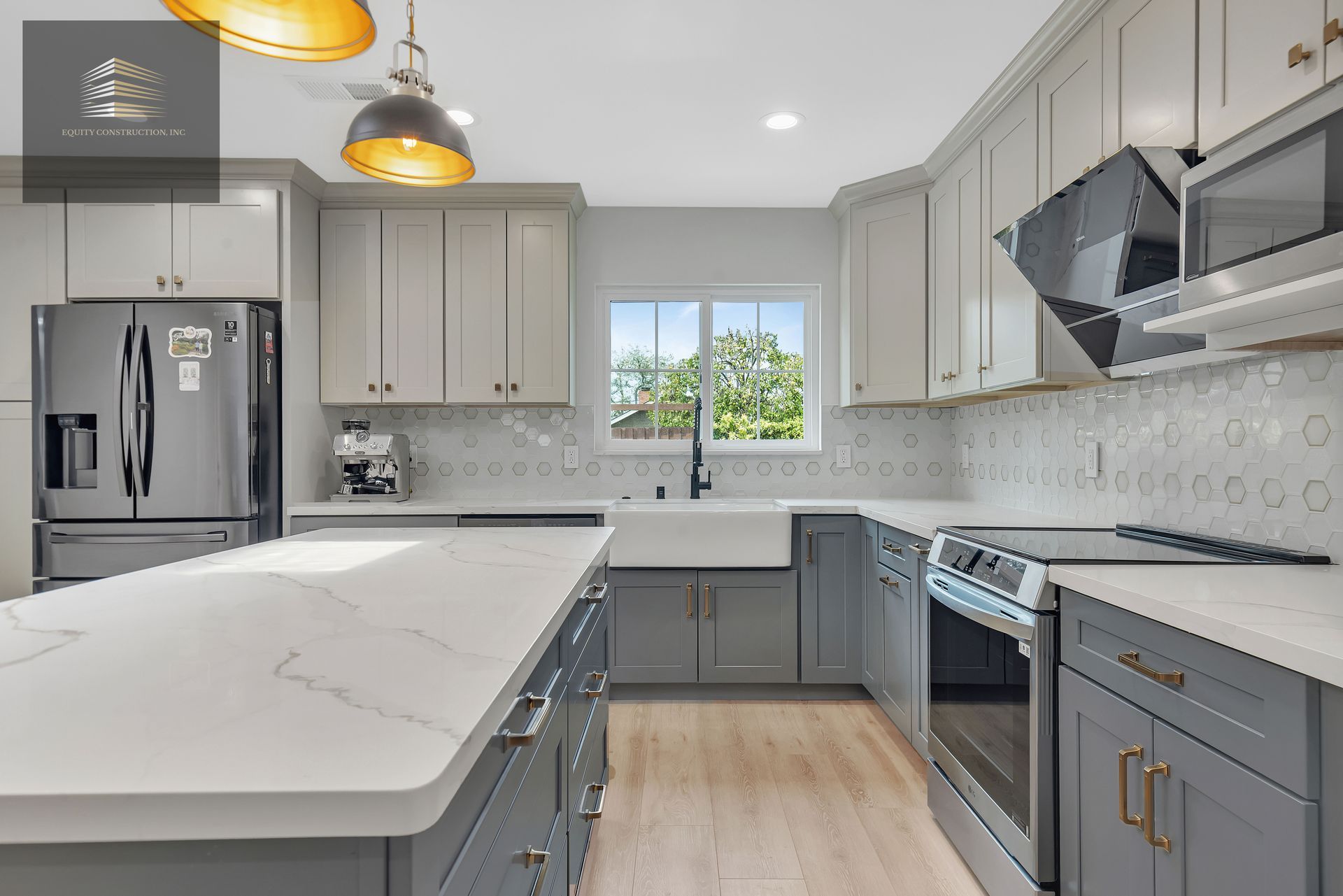 Modern kitchen with gray and white cabinets, stainless steel appliances, and large island.