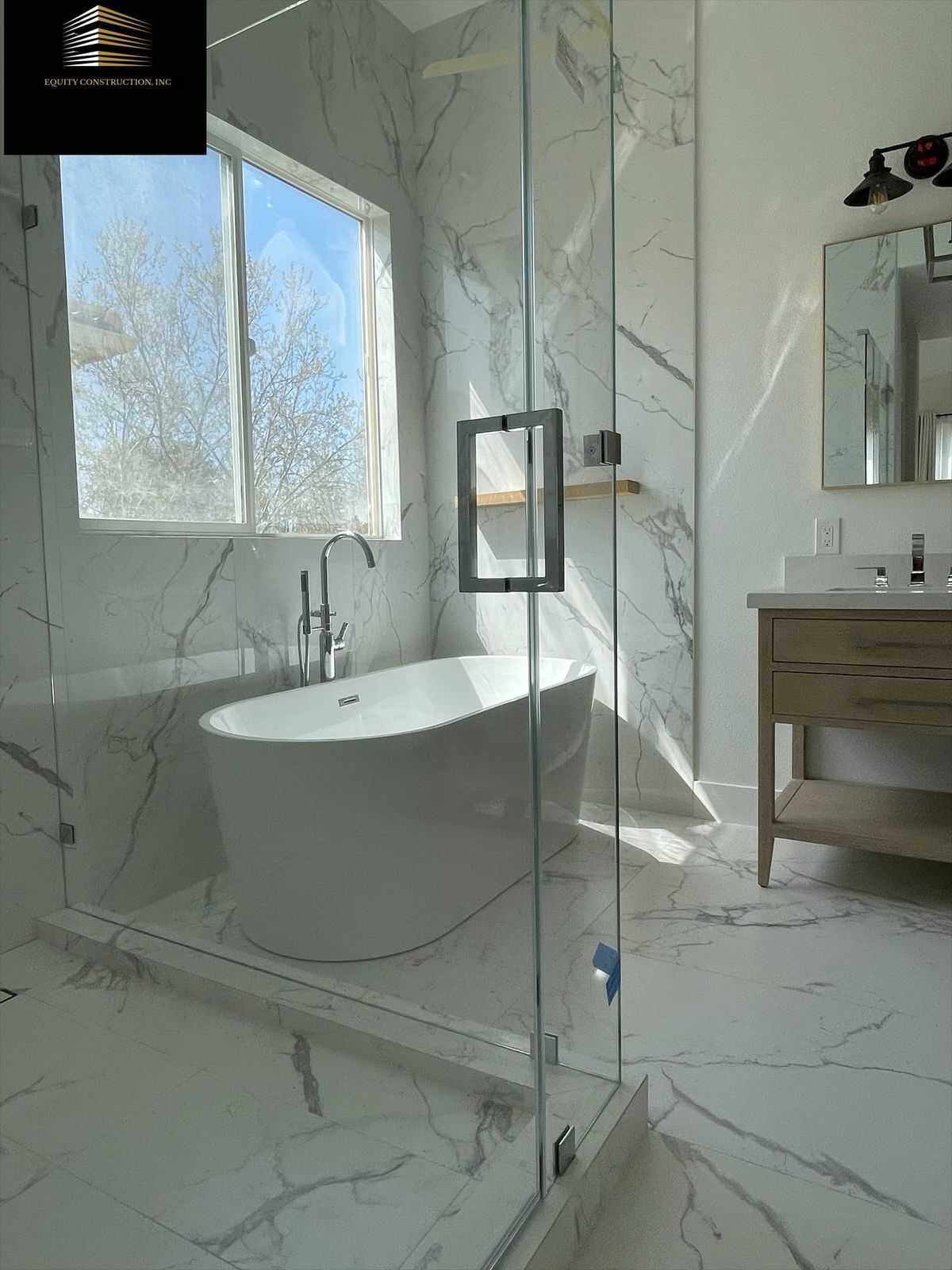 Modern gray-tiled shower with glass door, black fixtures, built-in bench, and small window.