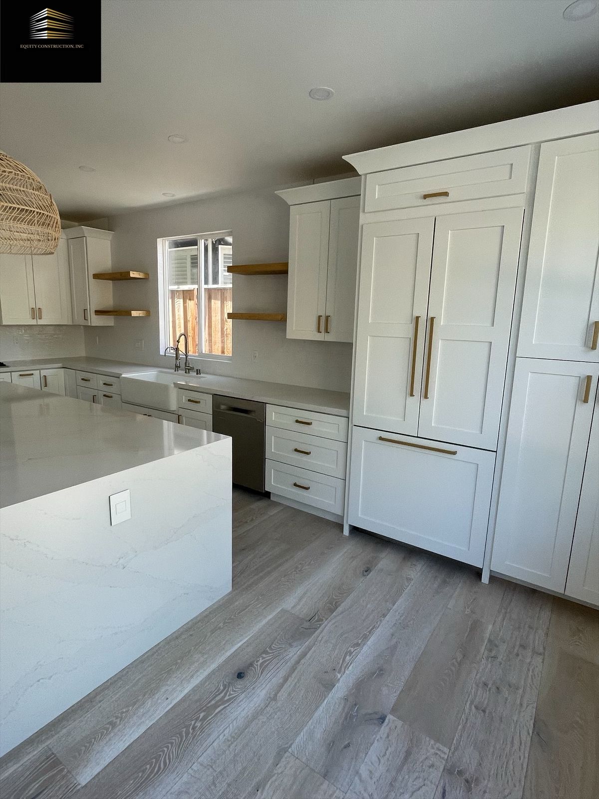 Modern white kitchen with island, cabinets, light wood floors, stainless steel appliances, and wooden shelves.