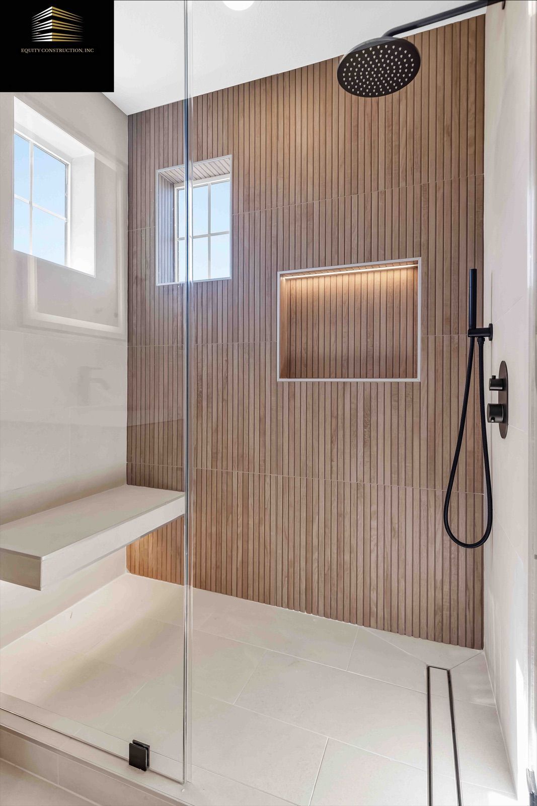 Modern shower with wood-look tile, glass door, bench, and black fixtures.
