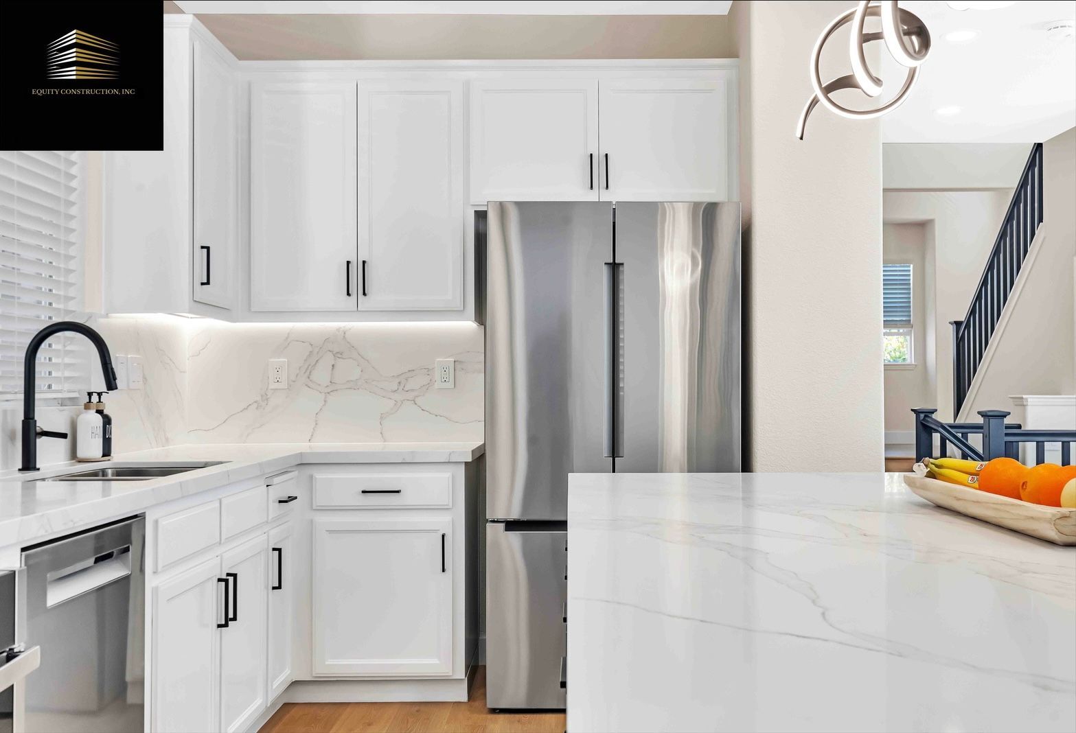 White kitchen with stainless steel refrigerator, marble countertops, and black hardware.