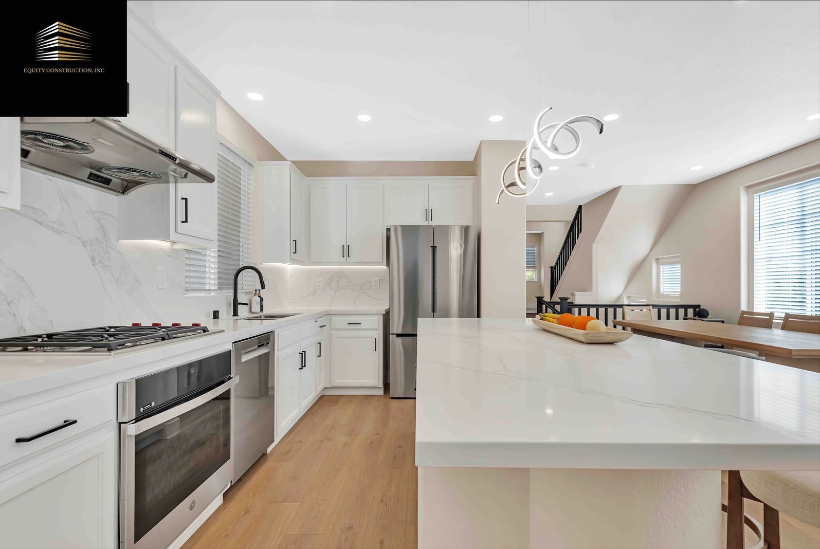 Modern white kitchen with stainless steel appliances, large island, and light wood flooring.