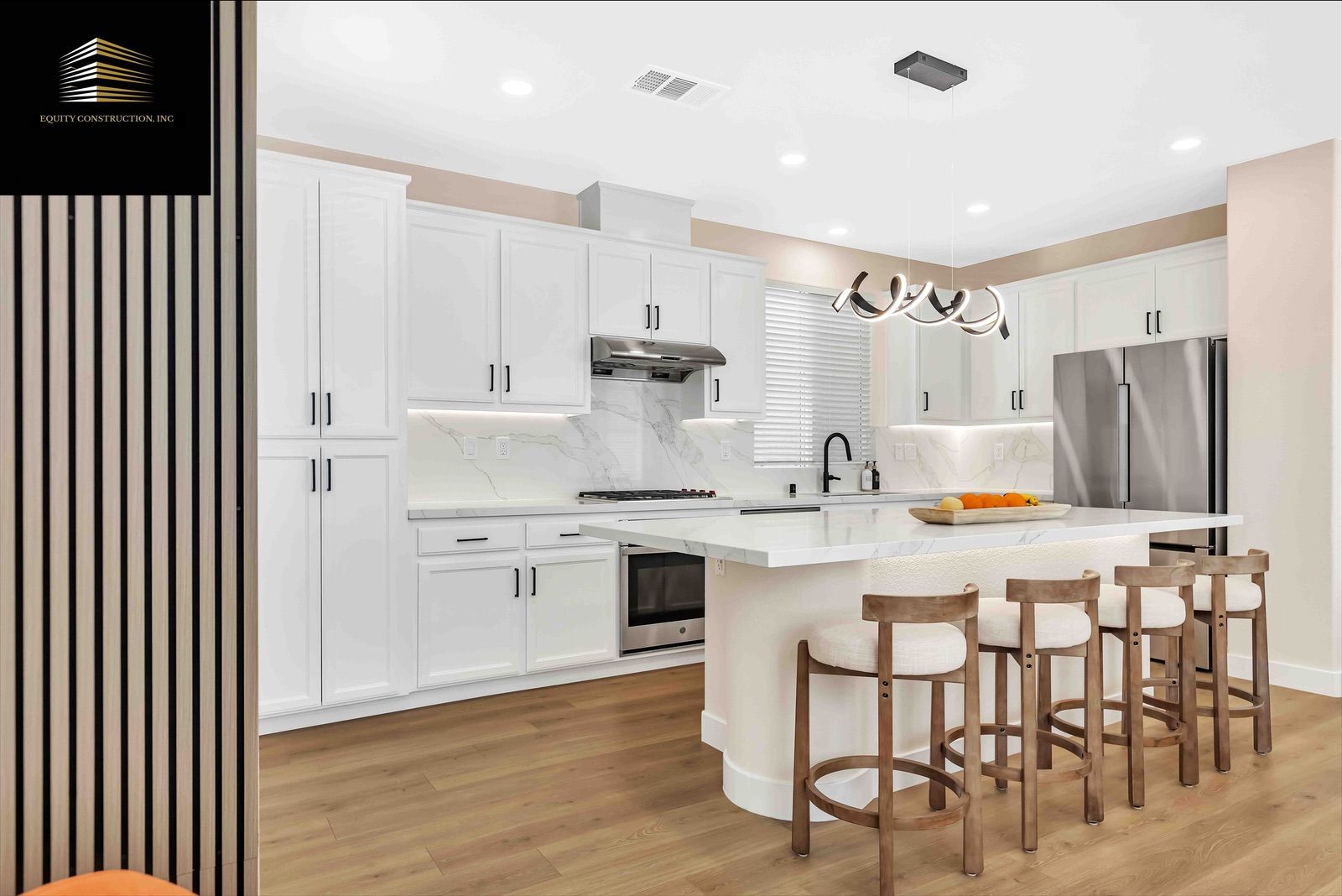 Modern white kitchen with island, bar stools, stainless steel appliances, and wooden floors.