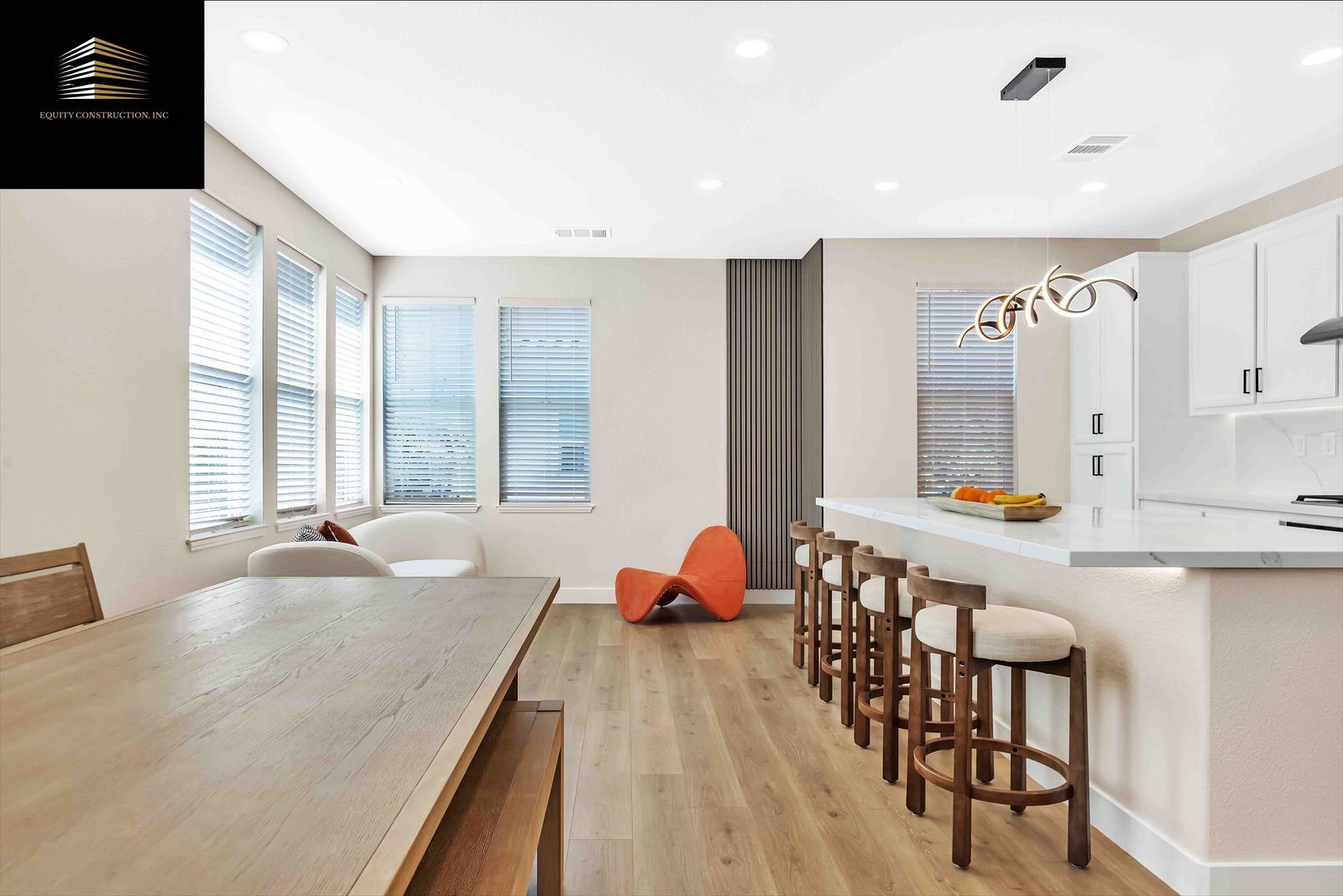 Interior view of a modern kitchen and dining area with wood floors, white cabinets, and an orange chair.