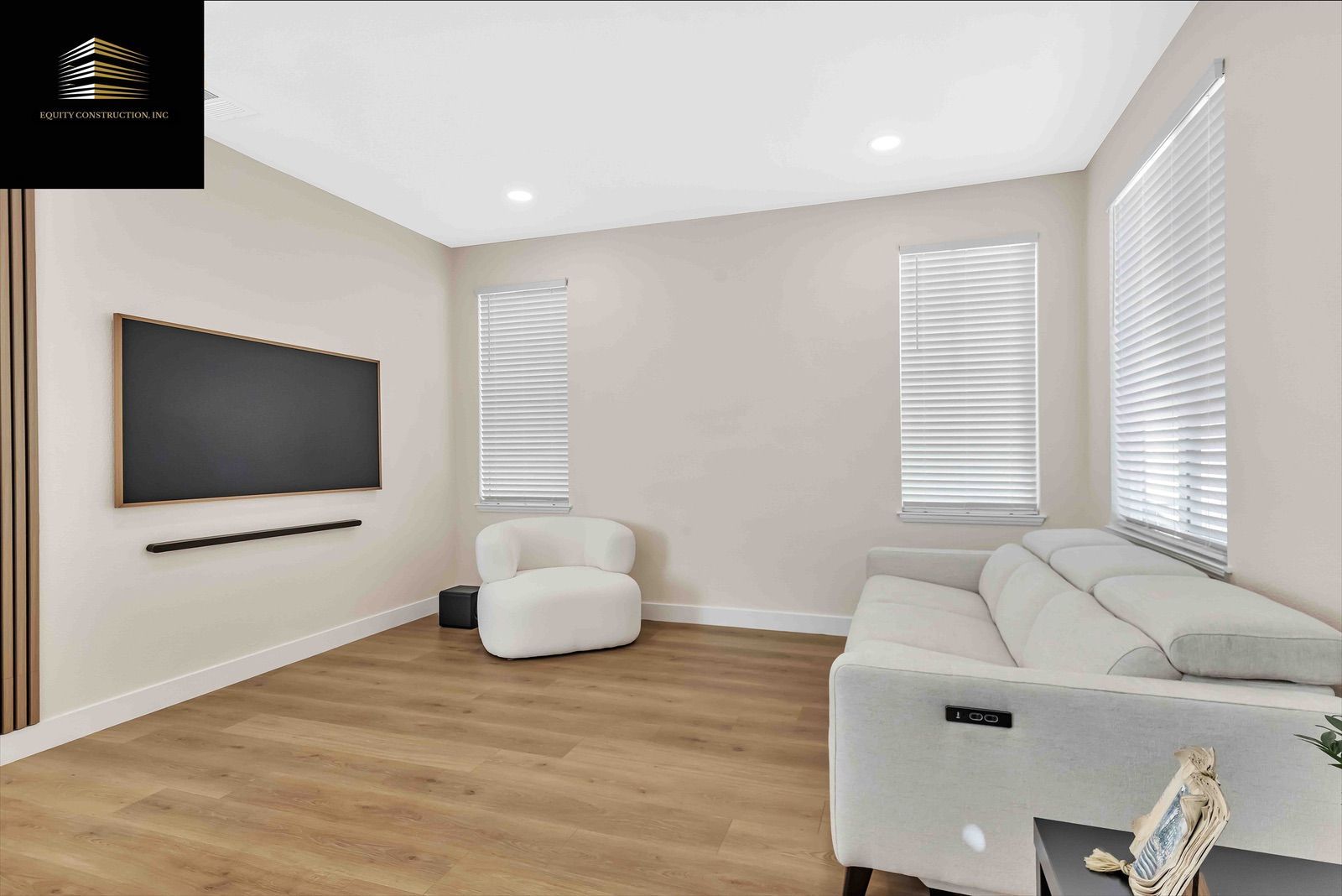 Empty living room with wood floors, TV, white couch, chair, and blinds.