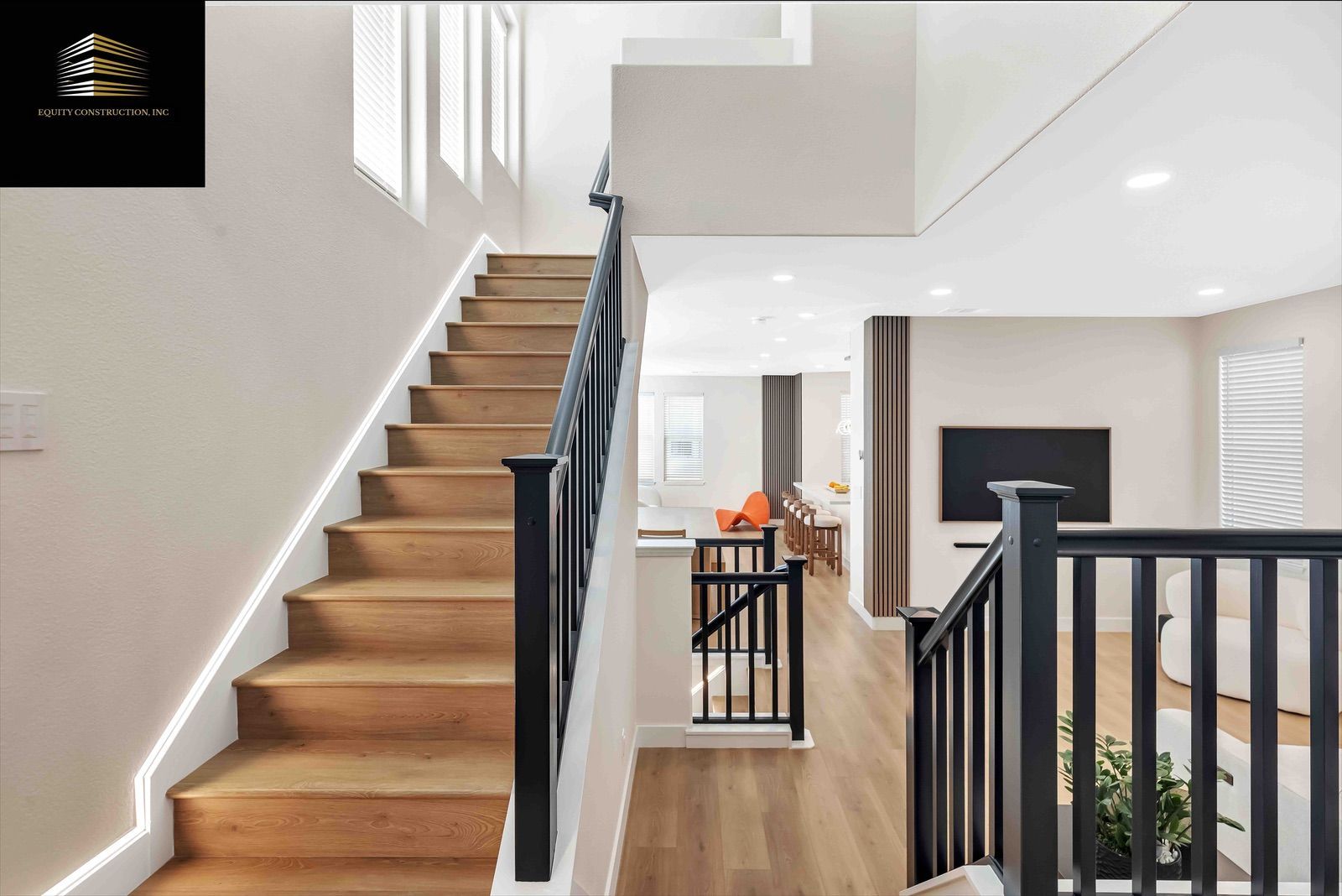 Wooden staircase with black railing leads to a living area with a TV and seating.