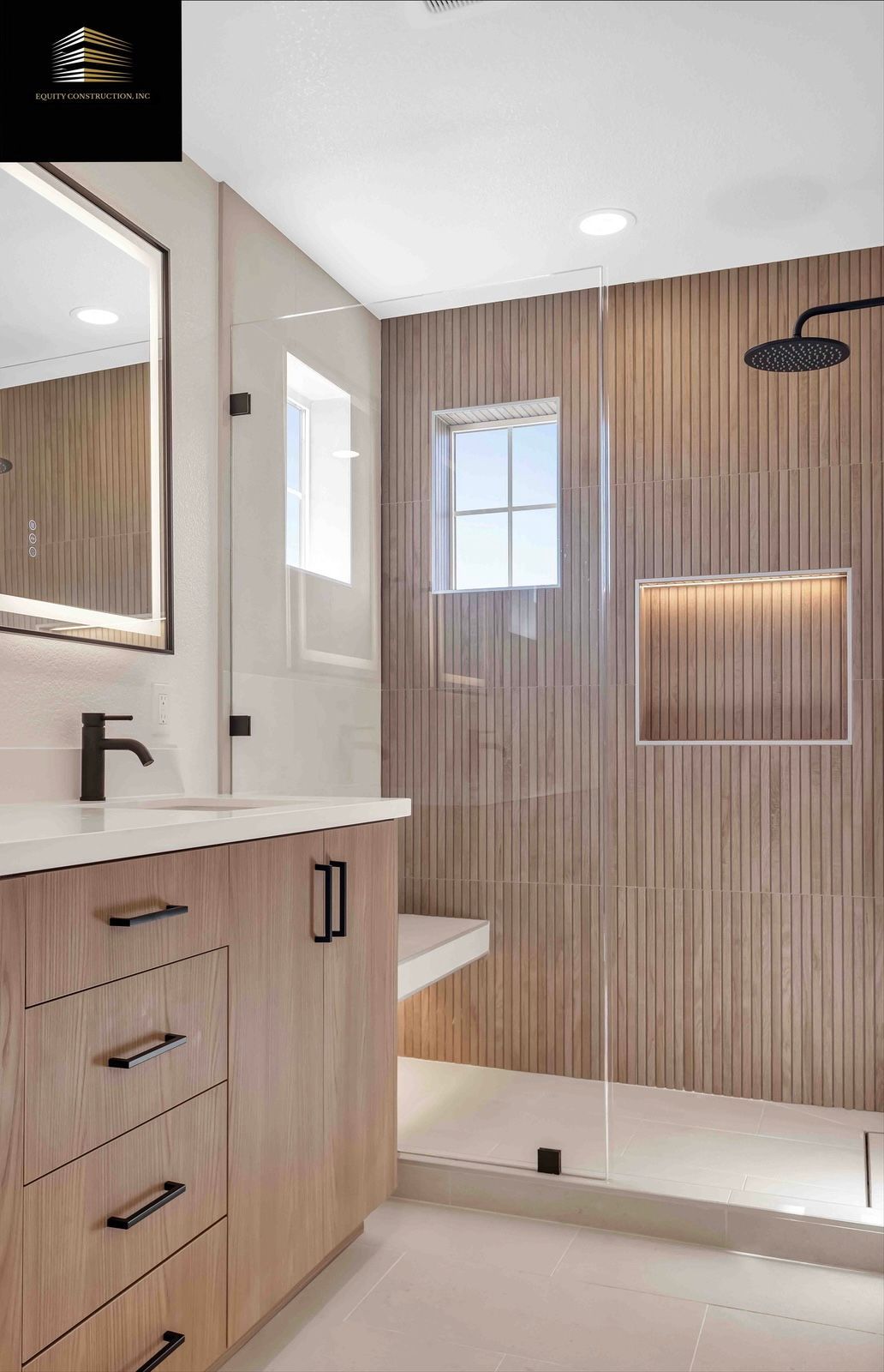 Modern bathroom: Light wood vanity, glass shower with bench, patterned wall tile, black fixtures.
