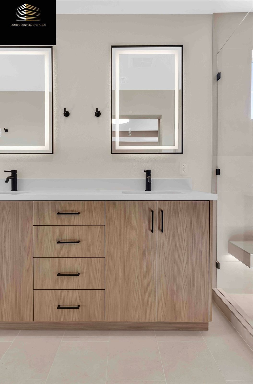 Bathroom with light wood vanity, black fixtures, and illuminated mirrors. Beige walls and tiled floor.