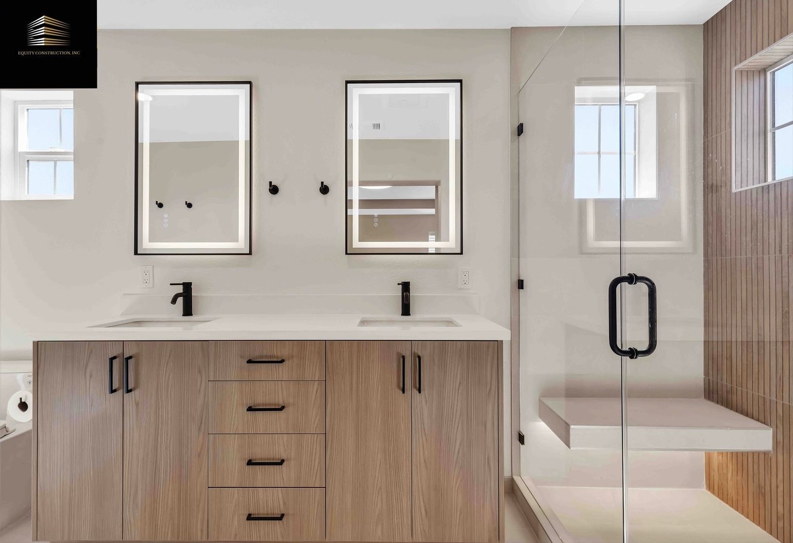Modern bathroom with double vanity, backlit mirrors, glass shower, and wood accents.