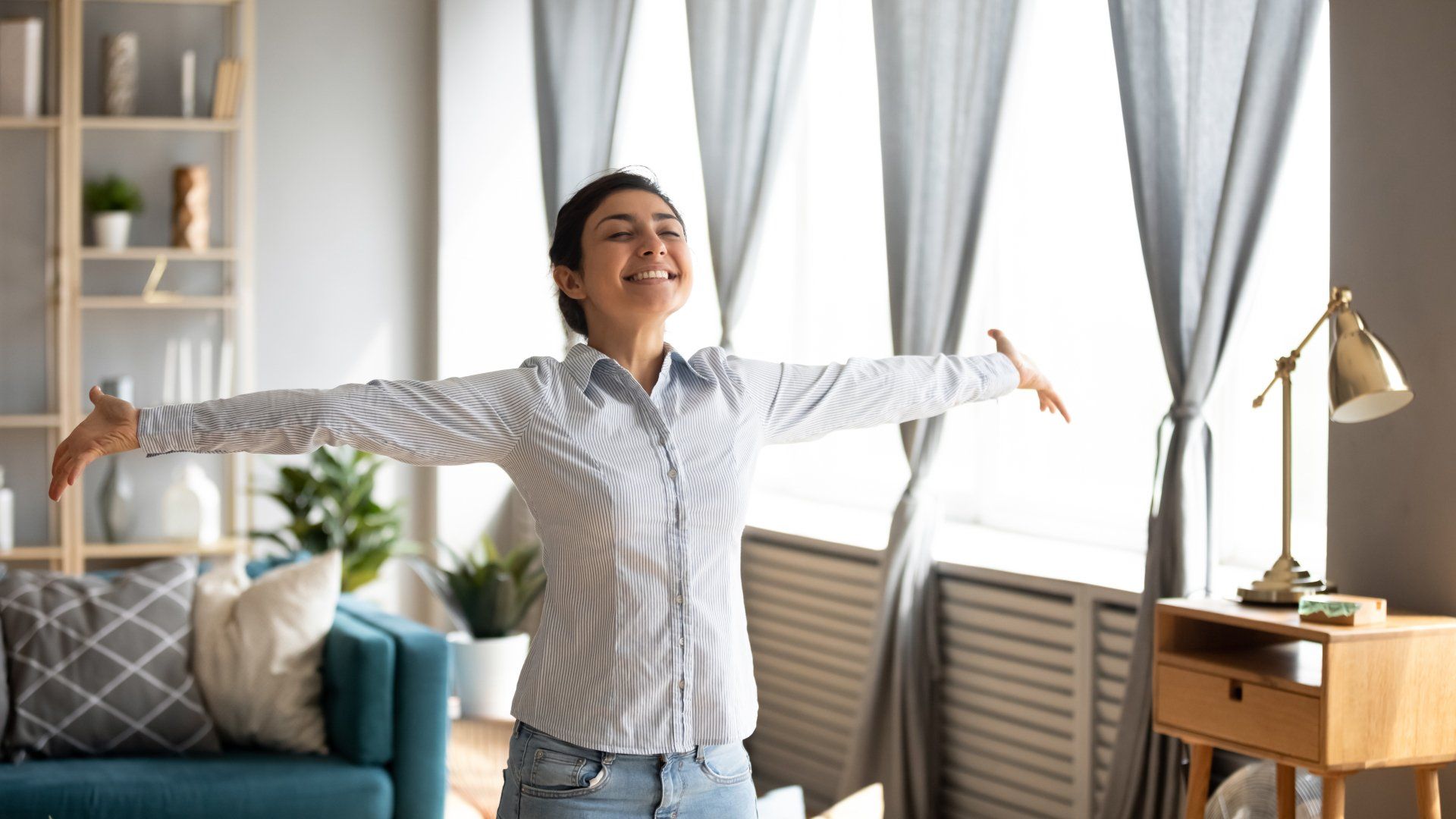 oung indian woman stand in modern living room interior with arms outstretched enjoy free lifestyle