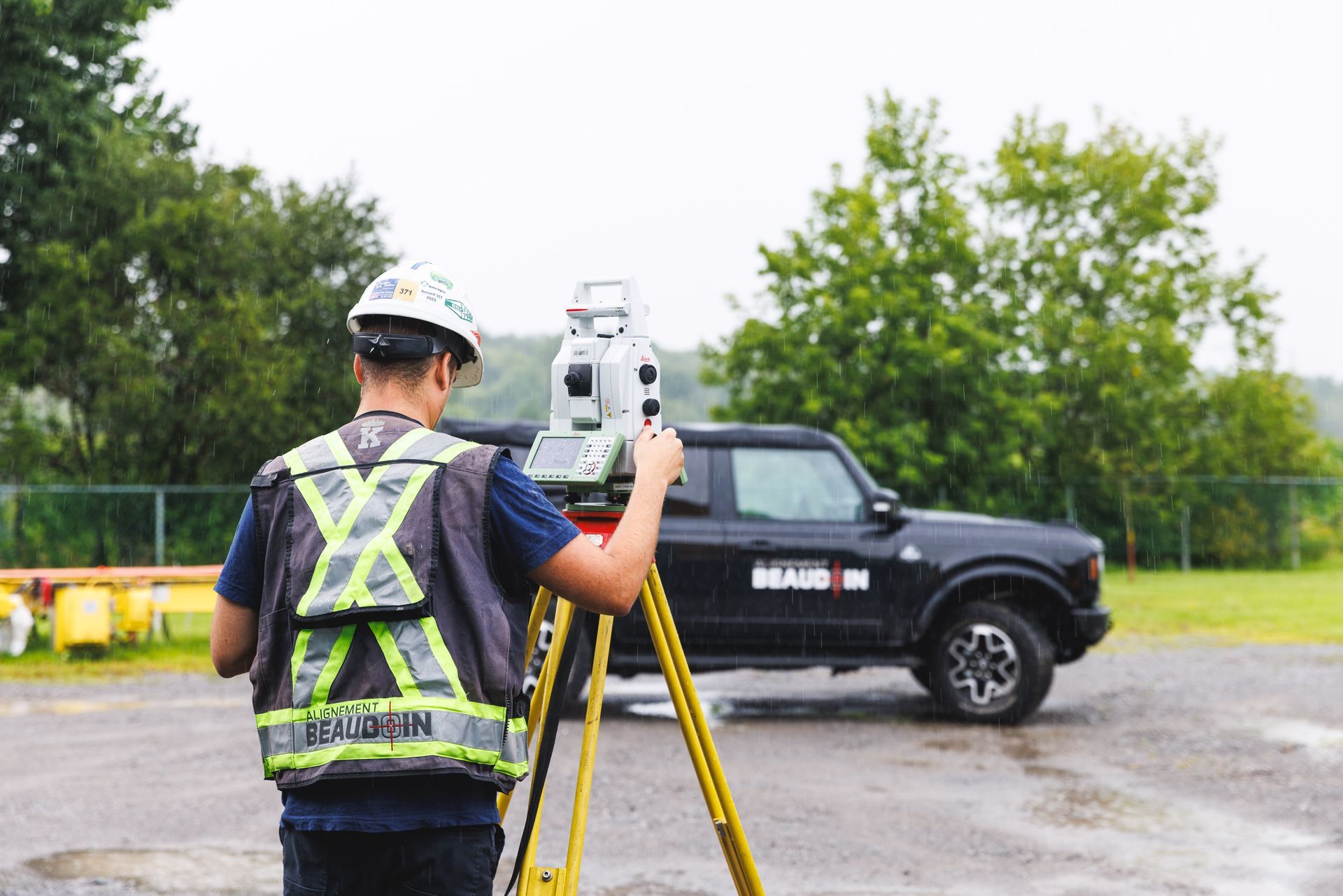 Un homme se tient devant un camion en utilisant une station totale.