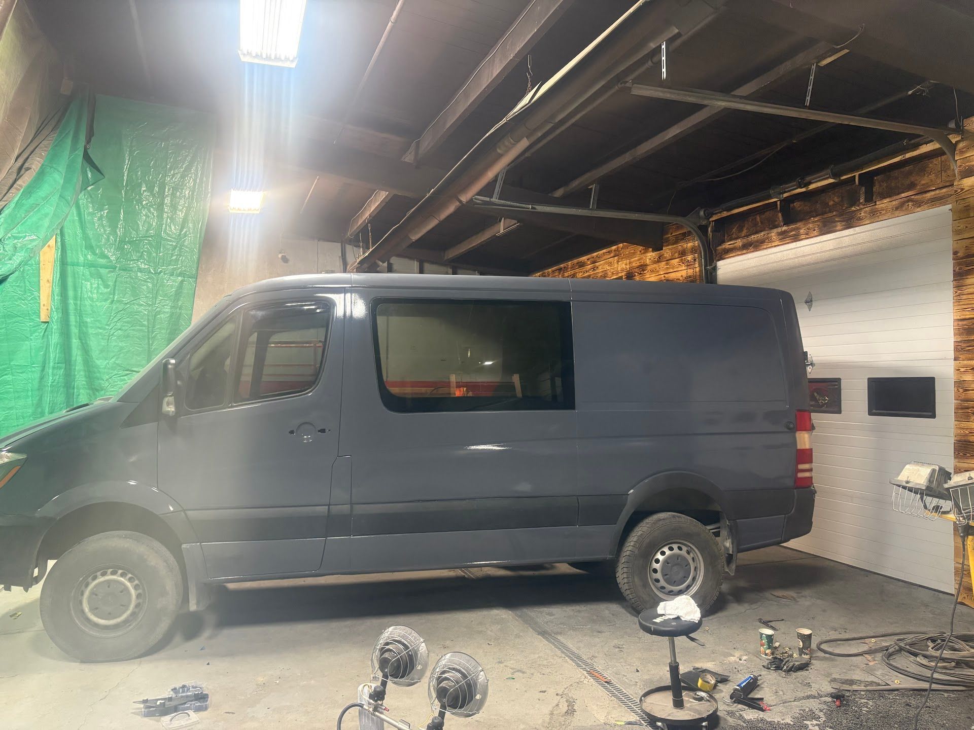 A blue van parked inside a workshop. The van is near a white brick wall and has a large tinted window. | Mega City Auto Niagara