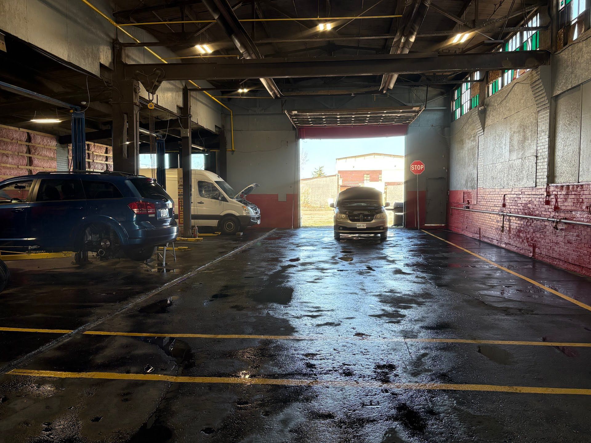 Inside a mechanic's garage with vehicles, the open door reveals bright daylight. The floor is wet. | Mega City Auto Niagara