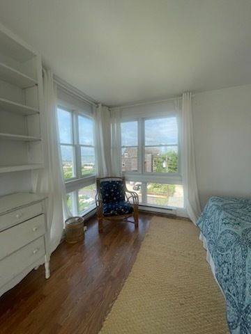 Bedroom with white walls, hardwood floor, and a window seat overlooking a city view.