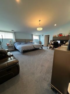 Large bedroom with a bed, desk area, and seating. Blue walls, gray carpet.