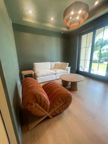 A living room with an orange chair, white sofa, wood coffee table, and large windows.