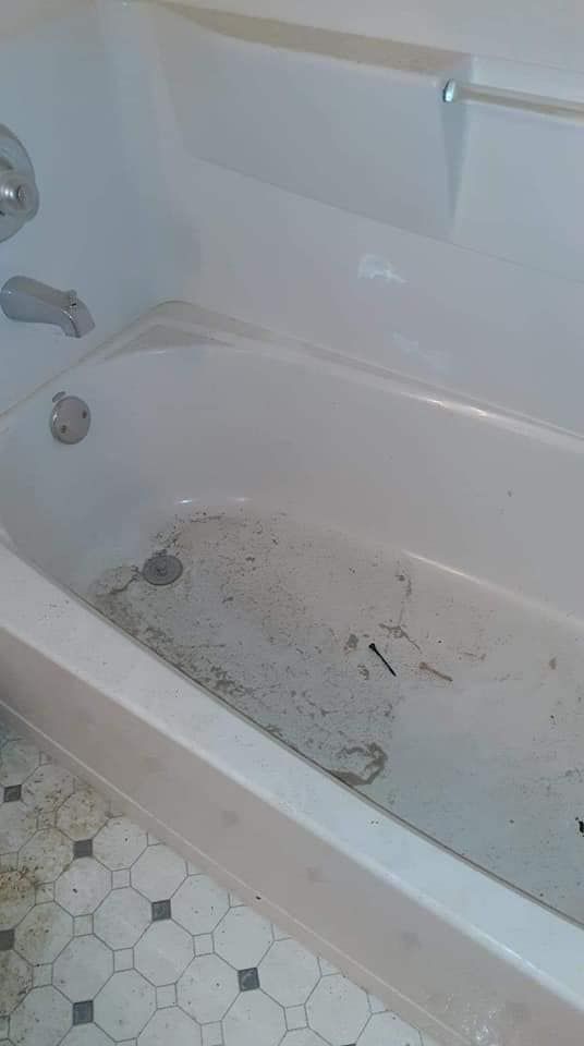 A dirty bathtub in a bathroom with a tiled floor.