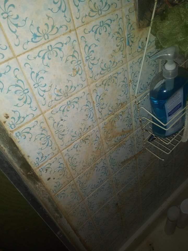 A dirty shower stall with a soap dispenser on the wall.