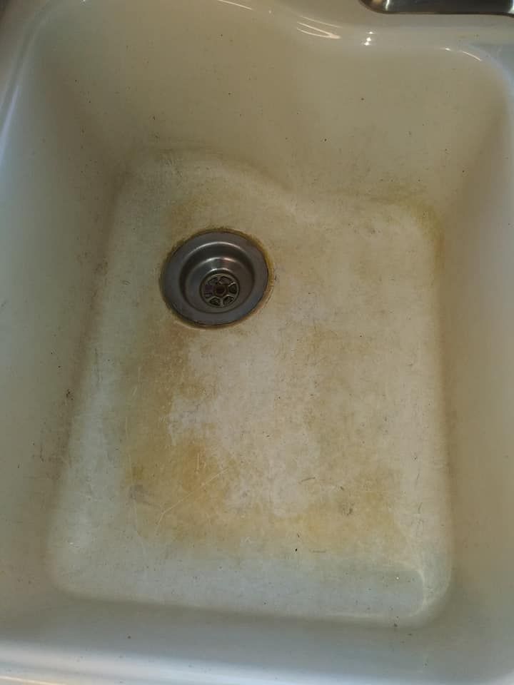 A close up of a dirty kitchen sink with a drain.