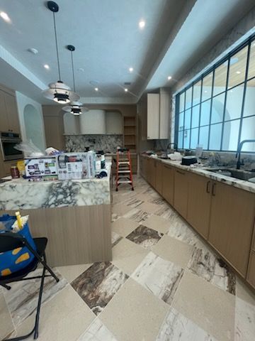 A kitchen undergoing renovation with marble countertops, light wood cabinets, and checkerboard floor tiles.