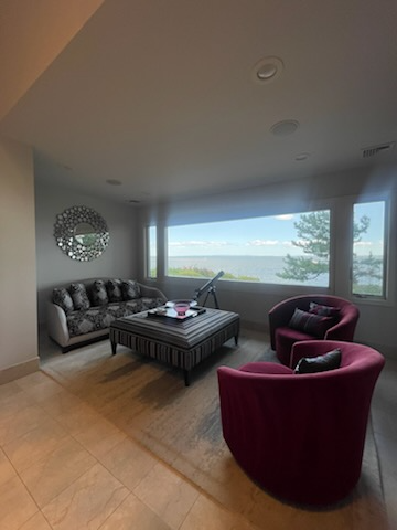Living room with lake view, floral sofa, striped ottoman, burgundy armchairs, mirror, and telescope.