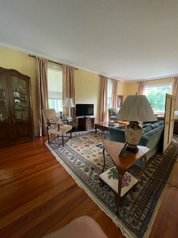 Living room with hardwood floor, area rug, and furniture; includes a blue sofa, chair, and a display cabinet.