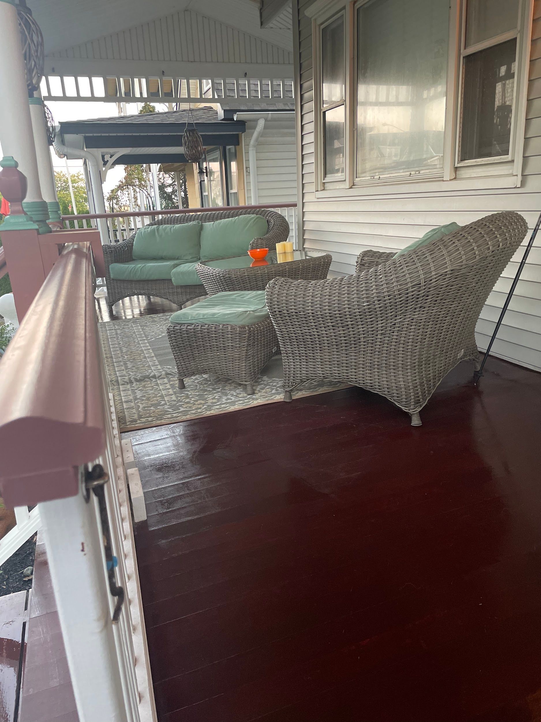 A porch with a couch , chair , ottoman and table.