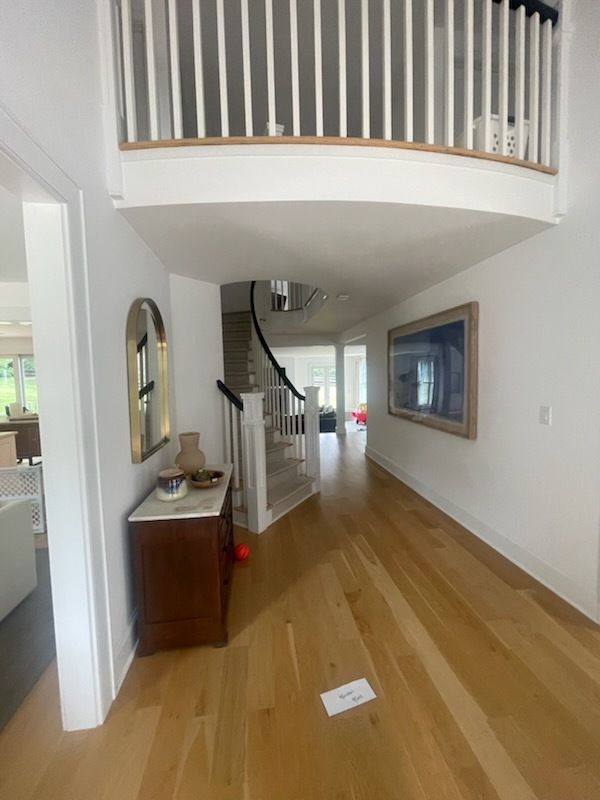 Hallway with light wood floors, white walls, and a staircase leading to the upper level.