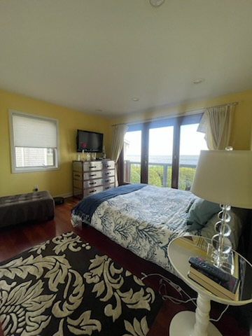 Bedroom with yellow walls, dark wood floors, and a bed with a blue and white comforter facing a scenic view.